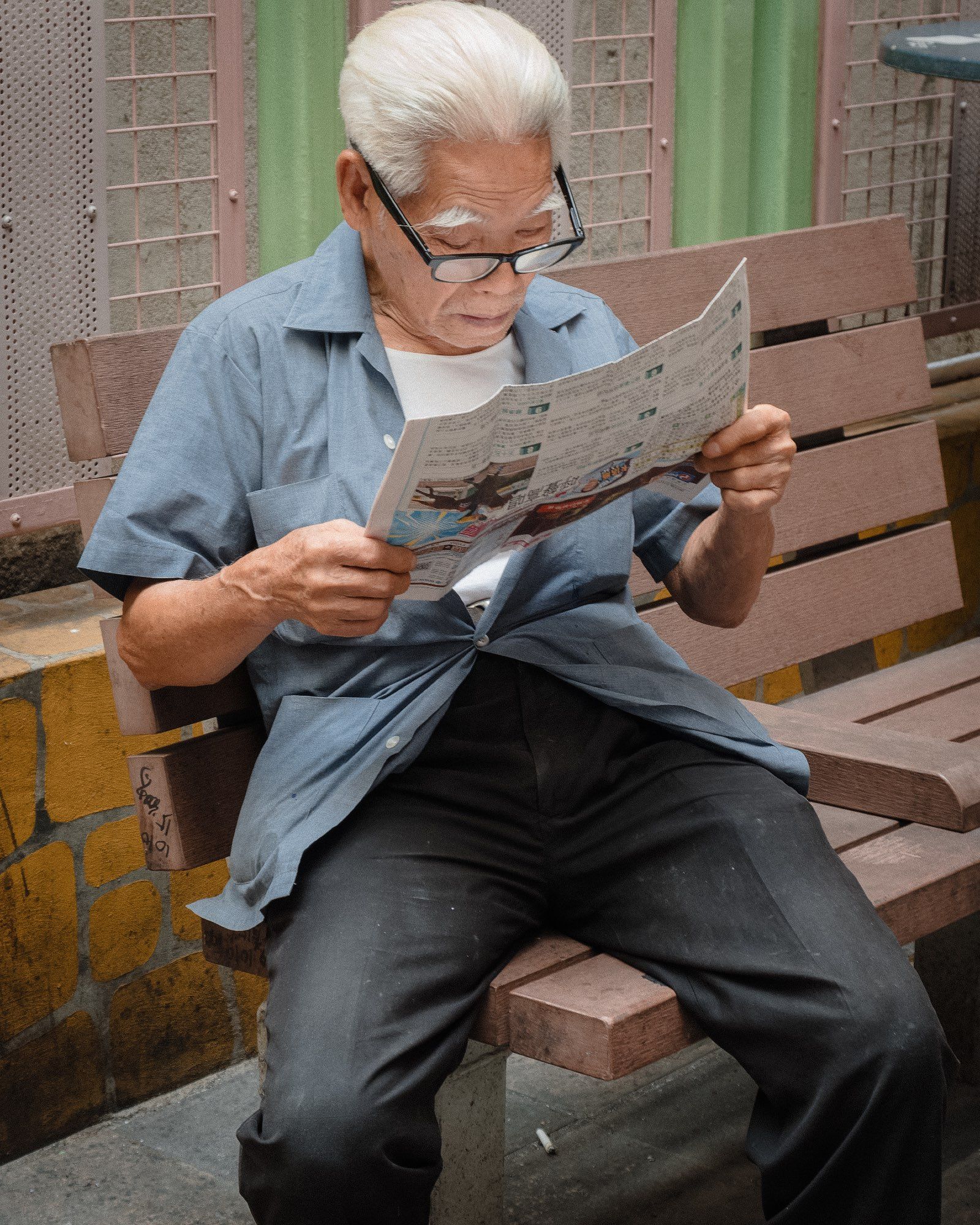 An older man reads the paper as the light bouncing off it illuminates his ample eyebrows and face.