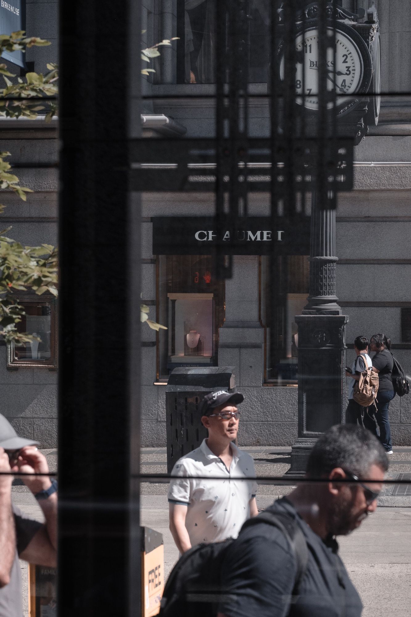 People milling to and fro in front of a jewelry store and clock.