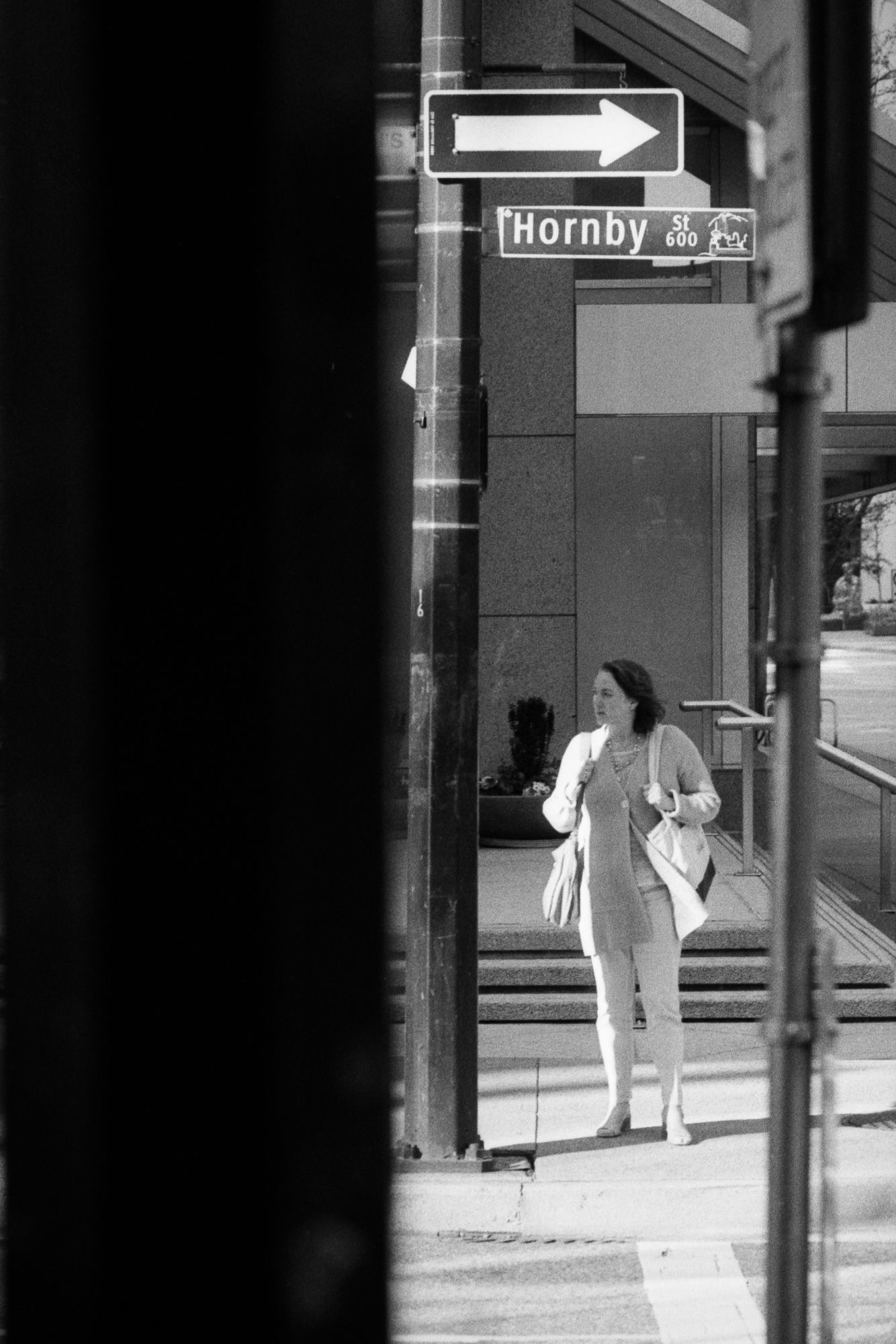 A woman looks the opposite way of a sign. Her clothing is blown in the direction of the sign.