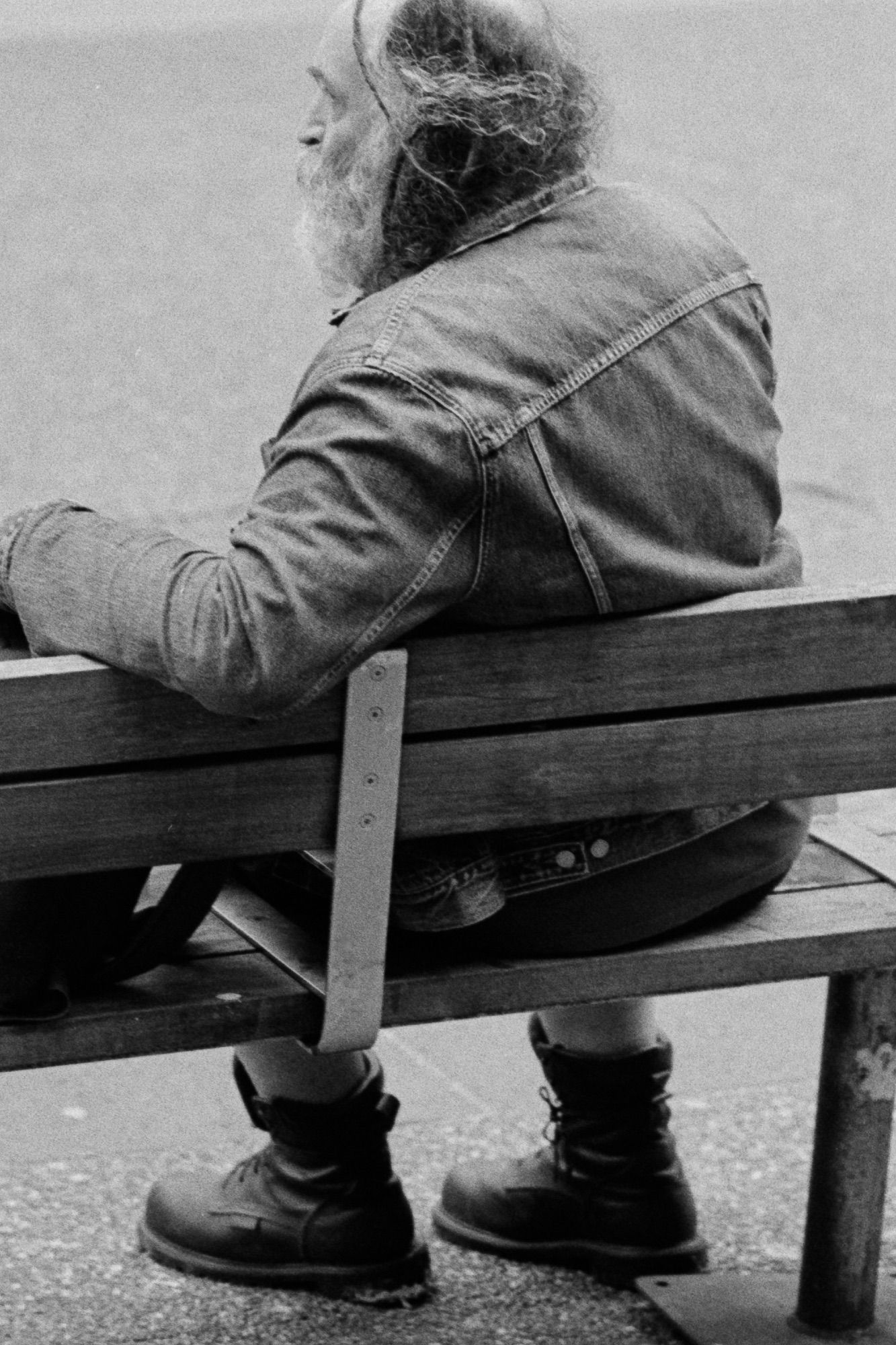 A man with heavy boots gazes out looking for his bus.