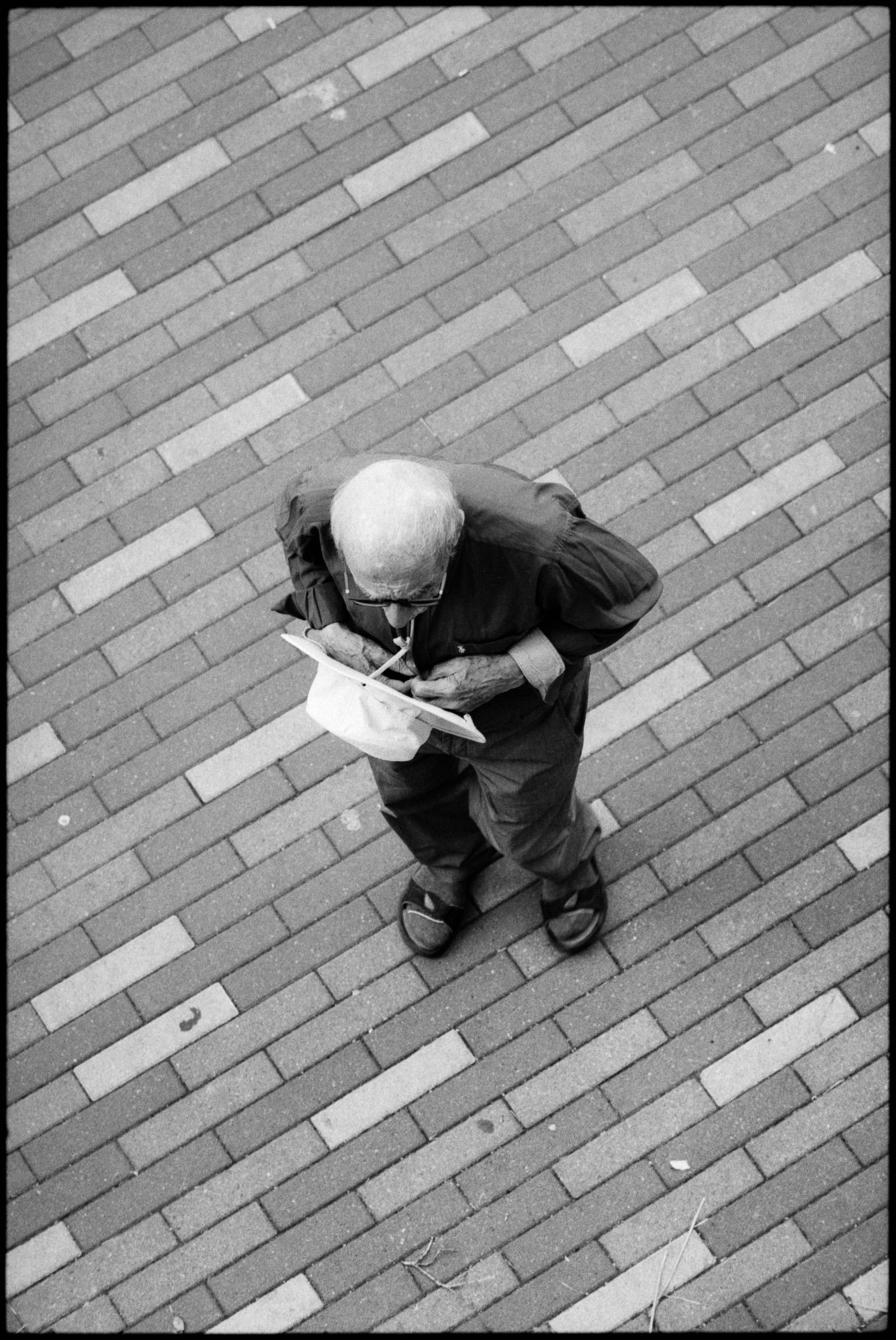 A man viewed from above clutches his hat and appears lost in thought.