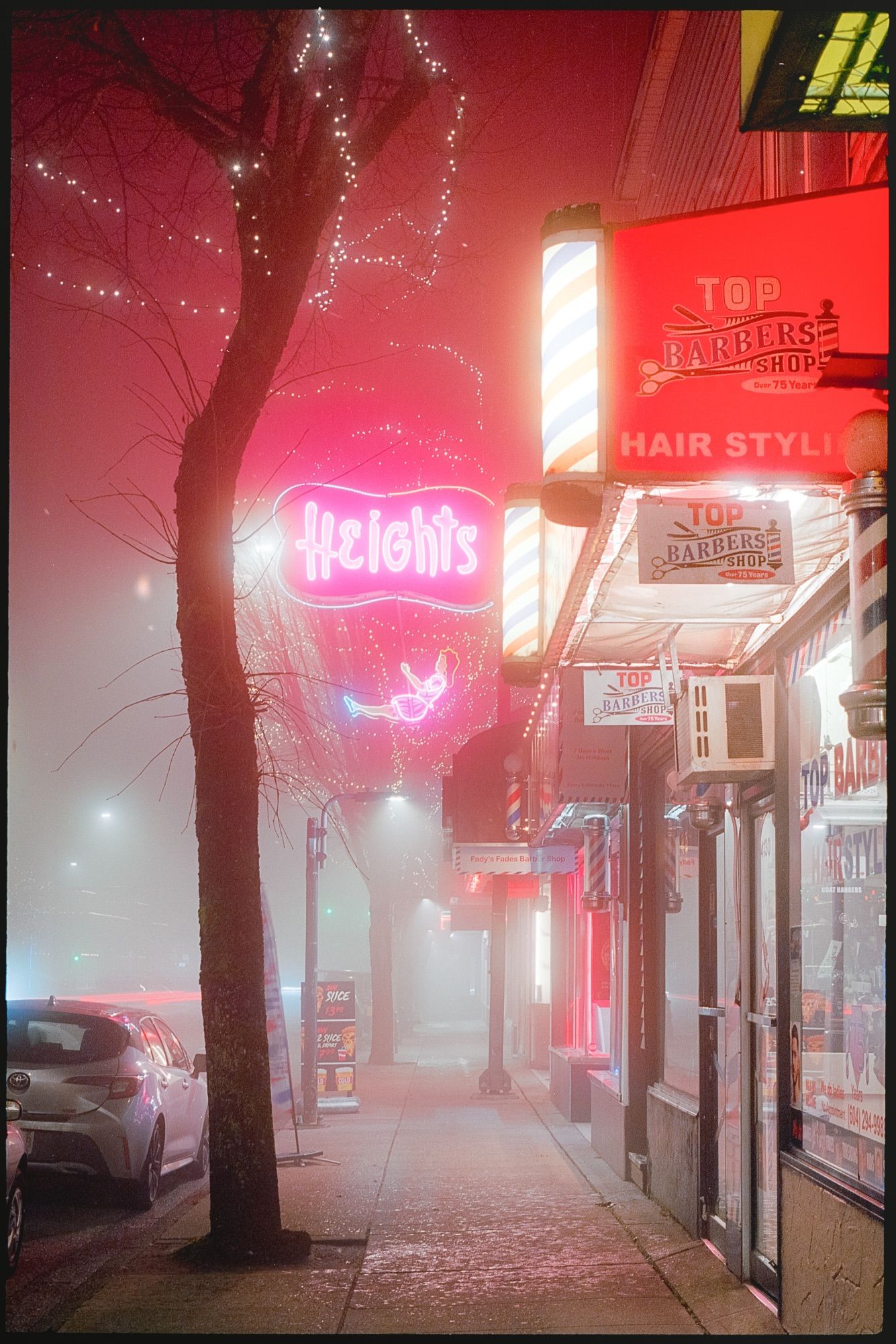 A neon sign glows in the distance behind a barbershop awning.