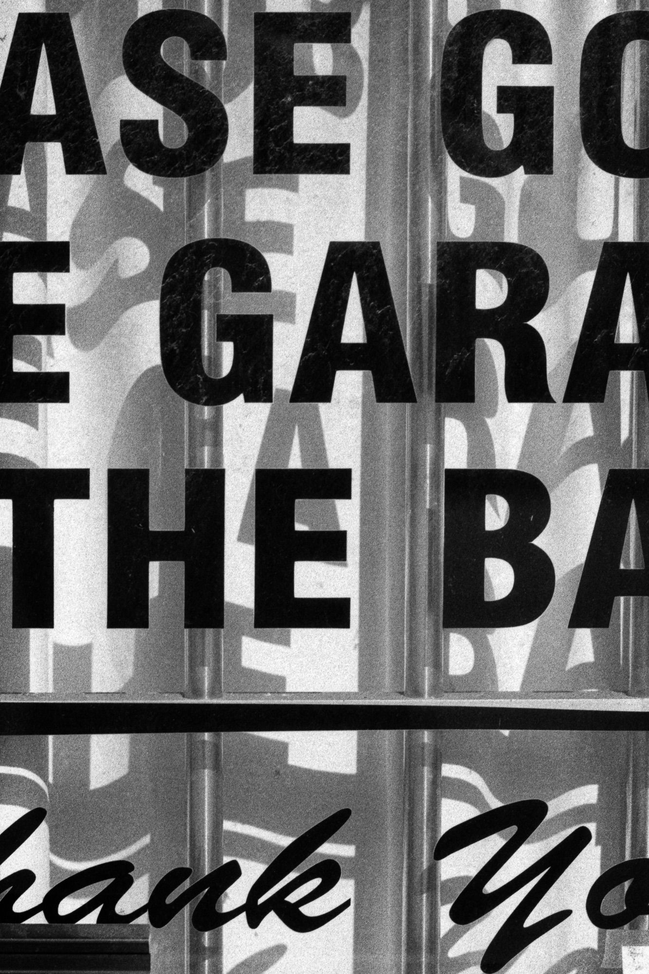 Black and white photographic detail of block letters on a storefront door with their shadows cast on a wave curtain.