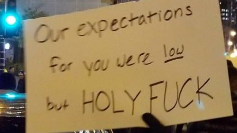 Sign at a protest at night taking up entire frame aaying"Our expectations for you were low but HOLY FUCK"