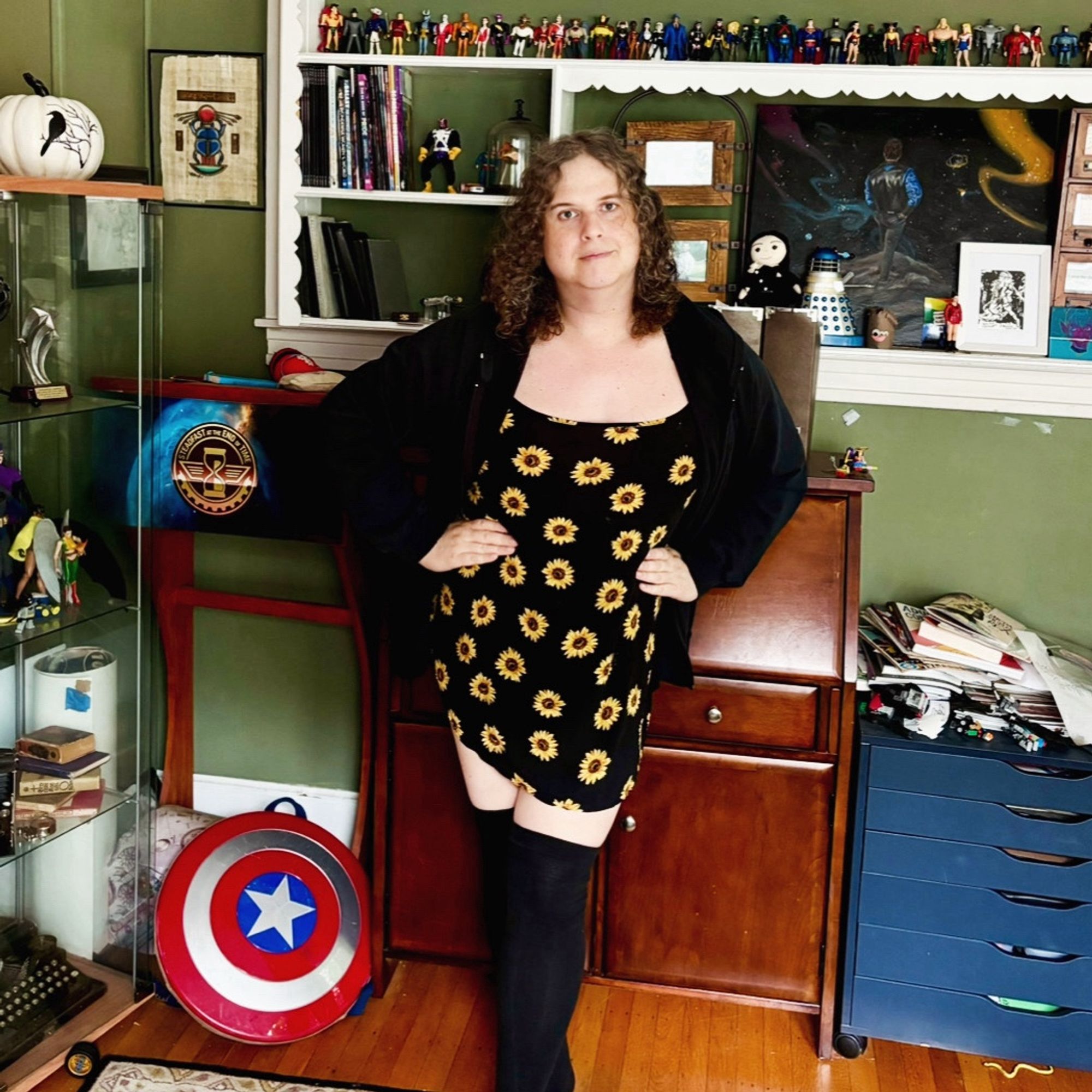 Jadzia is wearing a black hoodie over a short black sundress with sunflowers printed upon it, and thigh-high black socks.