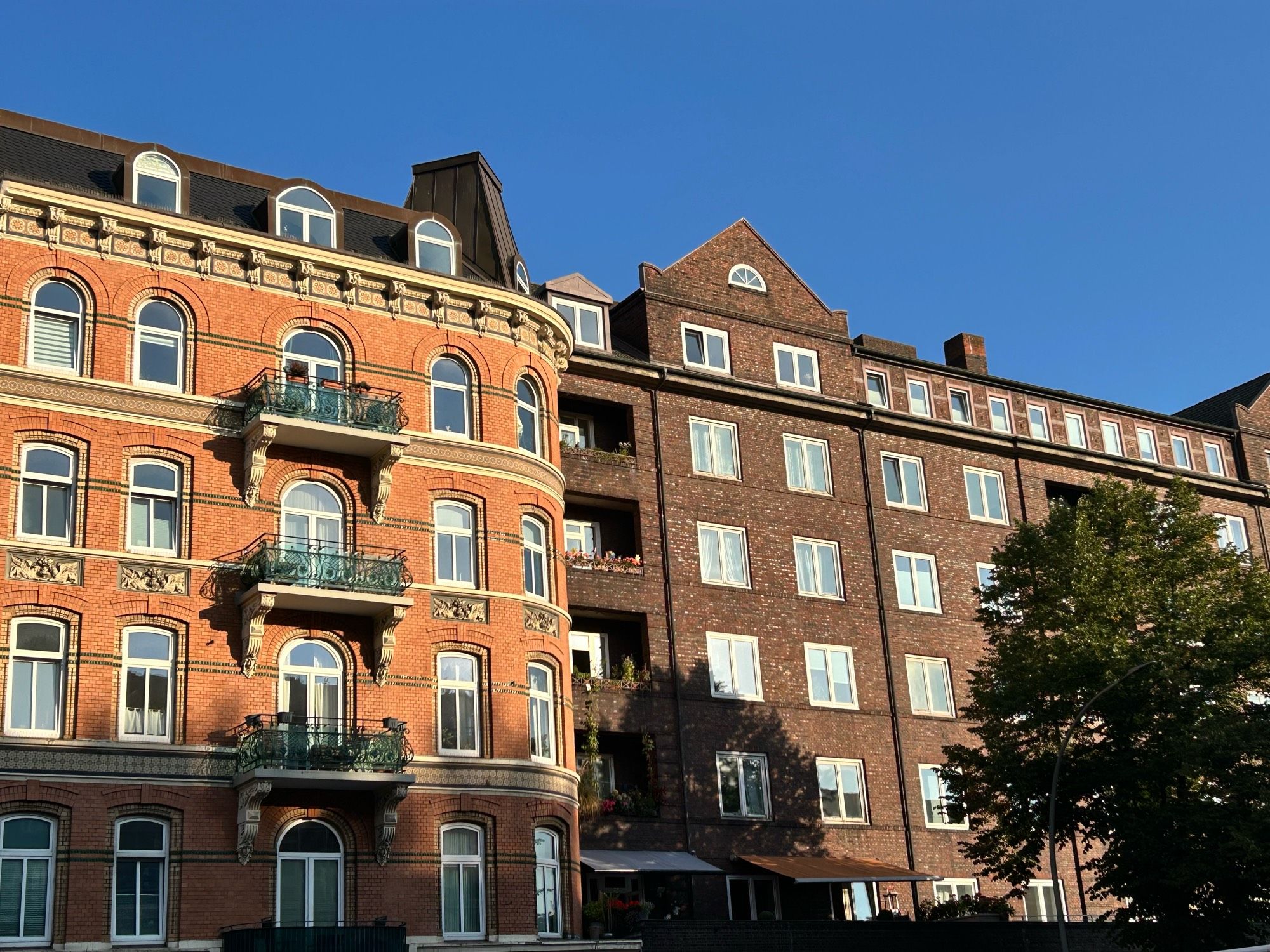 Backstein- und Jugendstil Haus nebeneinander, dahinter strahlend blauer Himmel.