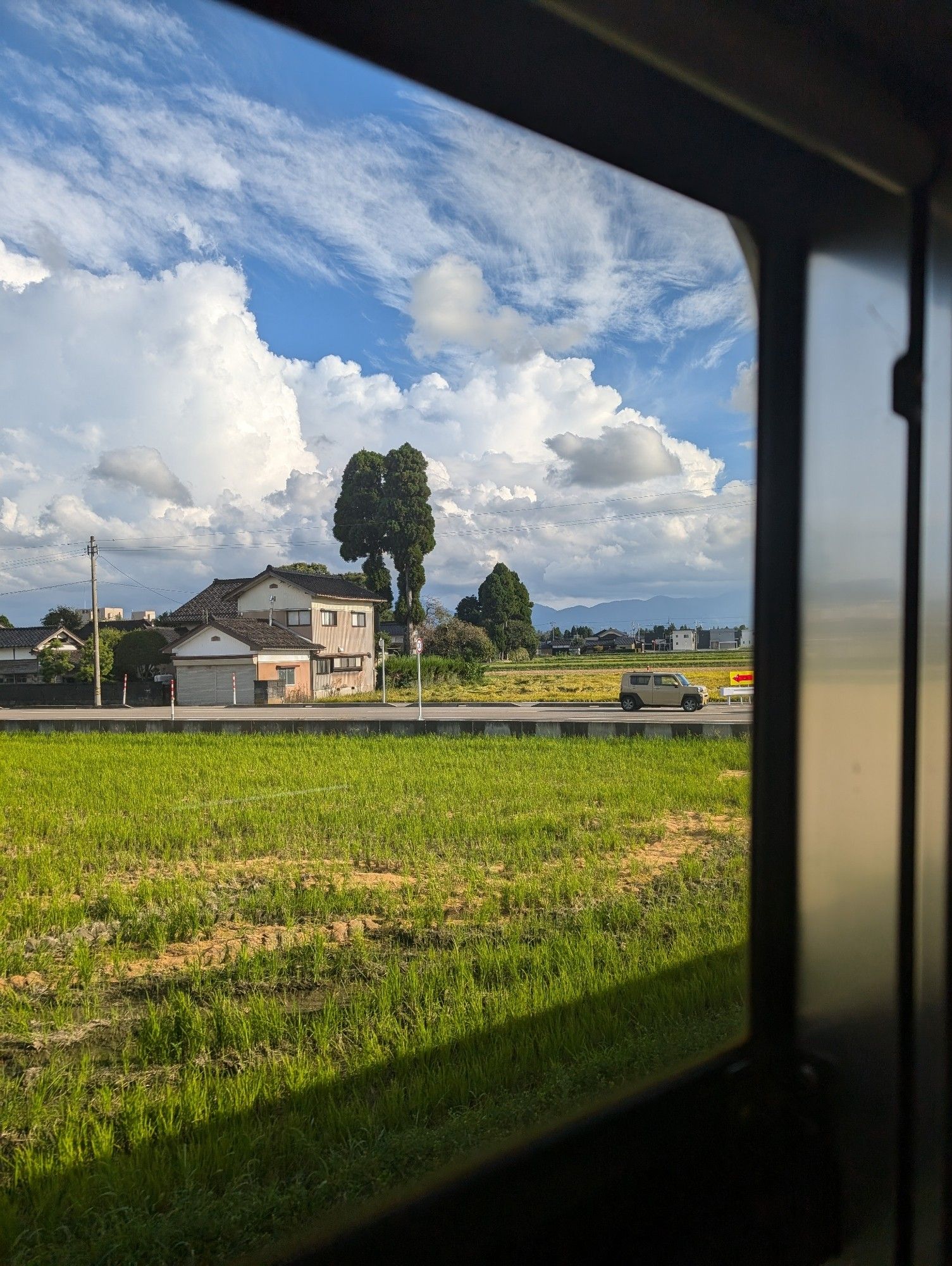 A photograph of rural Japan, somewhere between Takaoka and Johana, taken on a train. It's sunny :)