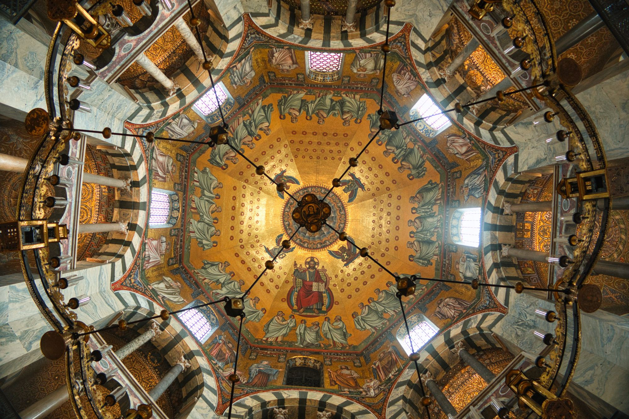 The interior of the highly ornate ninth-century Palatine Chapel in Aachen, looking through Frederik I's chandelier to the nineteenth-century dome mosaic.