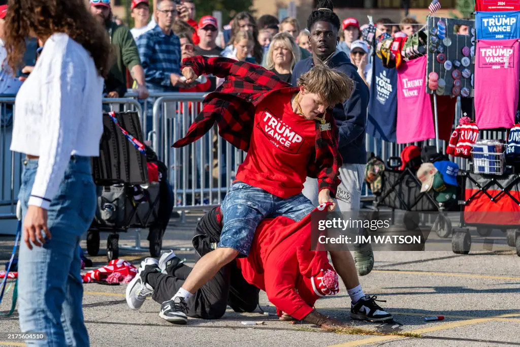 From Getty Images: Vendors selling Trump merchandise fight with each other before a campaign event with former US President and Republican presidential candidate Donald Trump at the Ryder Center for Health and Physical Education at Saginaw Valley State University in Saginaw, Michigan, October 3, 2024. (Photo by Jim WATSON / AFP) (Photo by JIM WATSON/AFP via Getty Images)