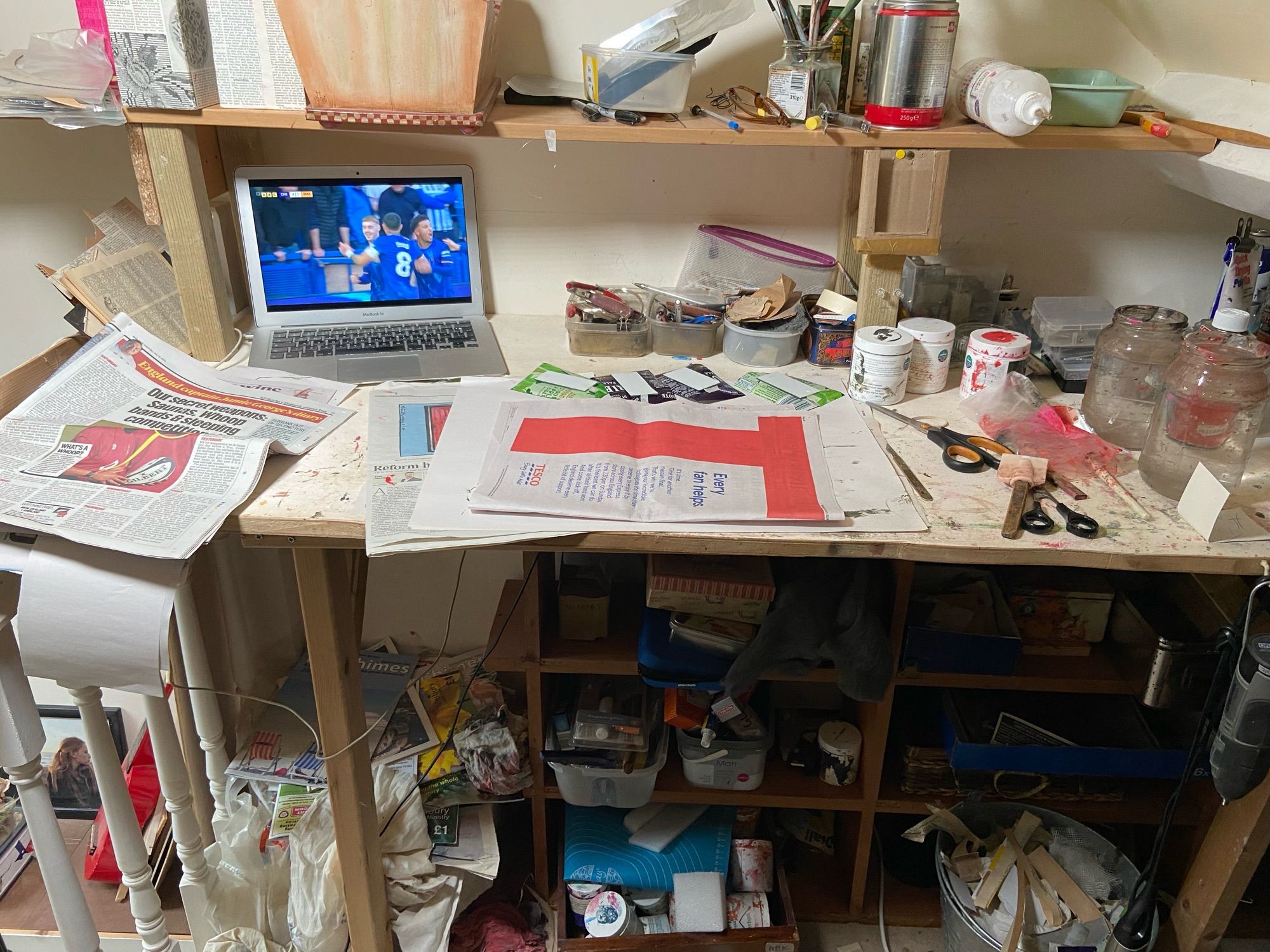 A very very messy desk with multiple glued, tools, papers and other materials