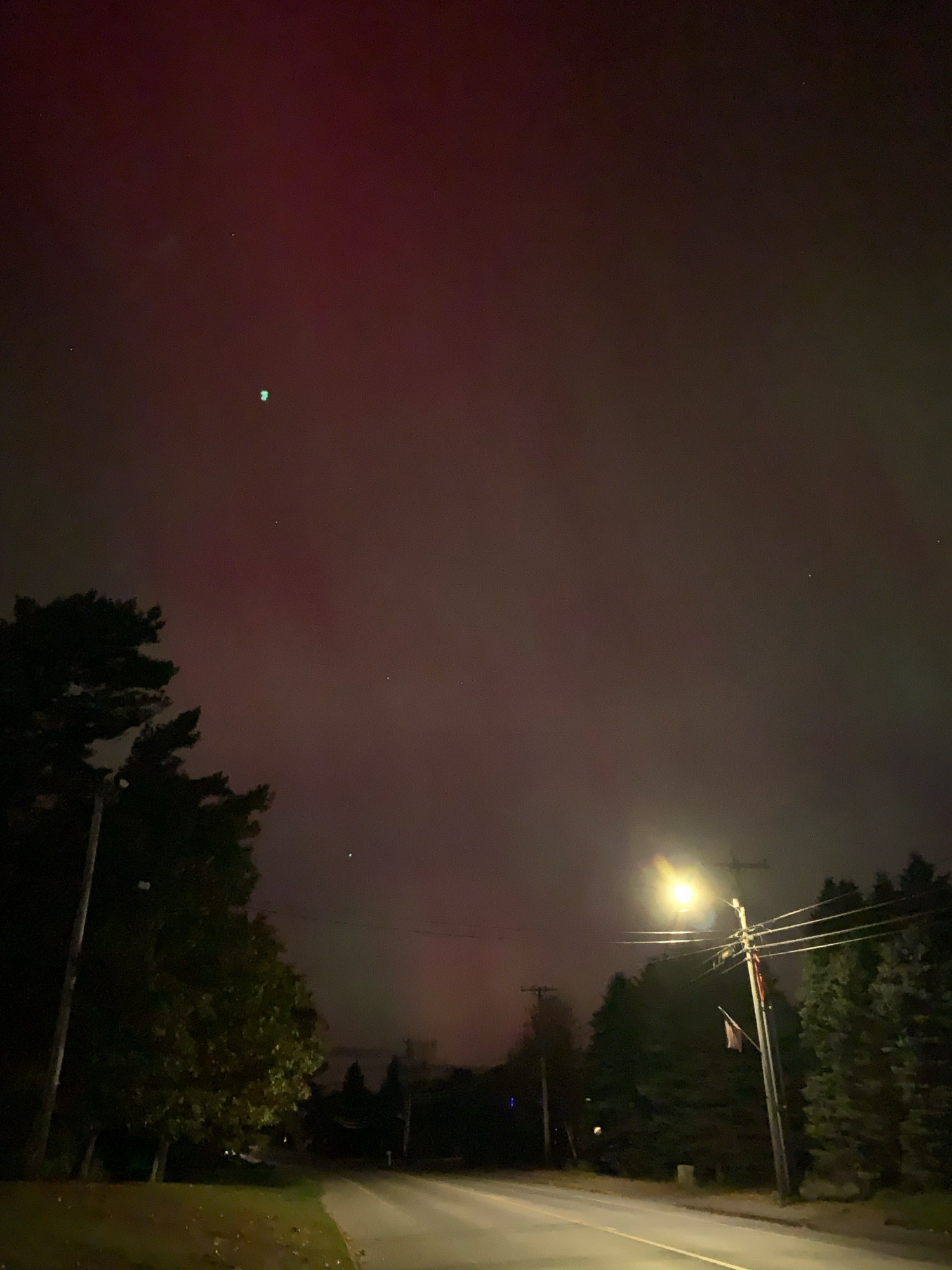 Photo of a dim red and green aurora borealis hovering over a partially lit road