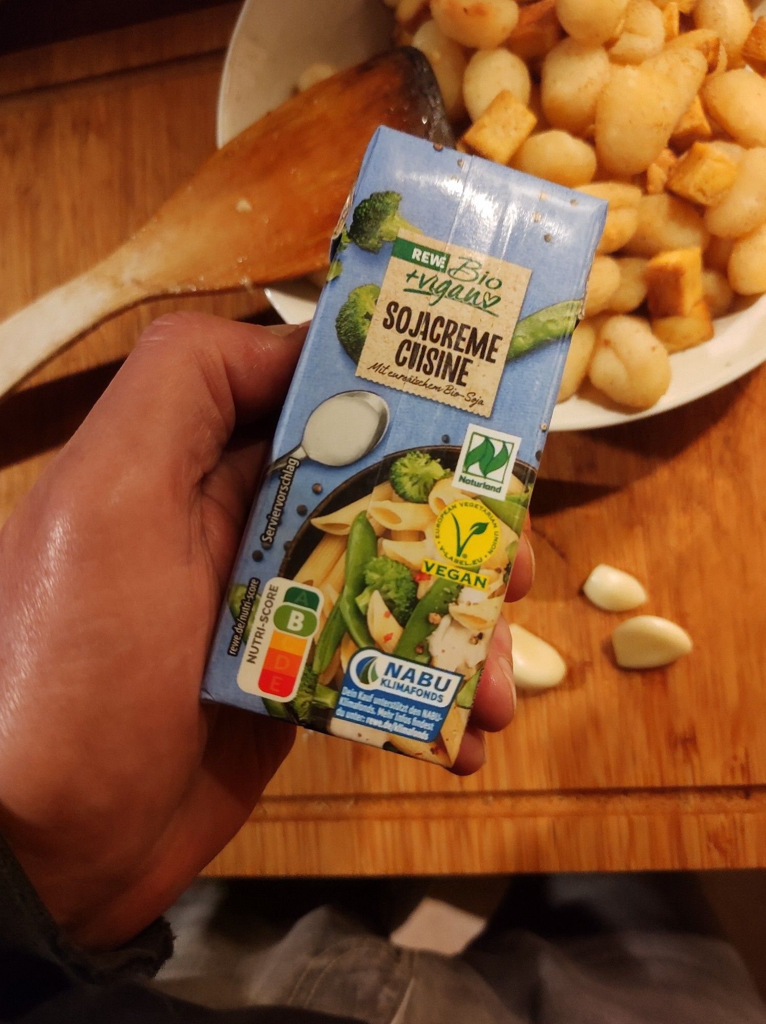 Veganes Rosenkohlgericht - Kleiner Tetrapak Sojacreme Cuisine von Rewe Bio über einem tiefen Teller, in dem die vorgebratene Gnocchi und der Räuchertofu auf den Rosenkohl in der Pfanne warten