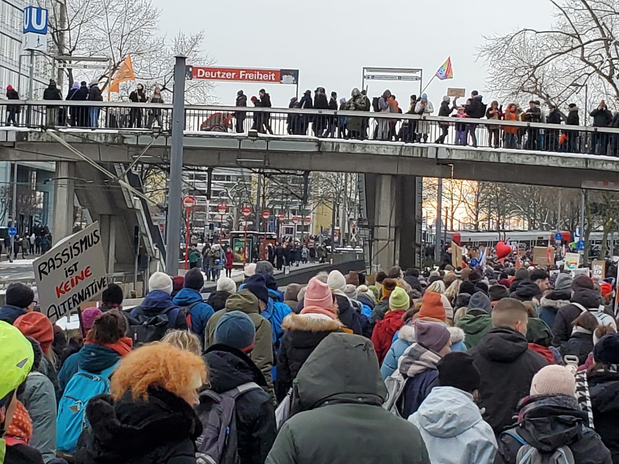 Demonstrators at today's protest. Many people are seen, in winter hats and jackets, several carrying signs, e.g., "Rassismus ist keine Alternative"