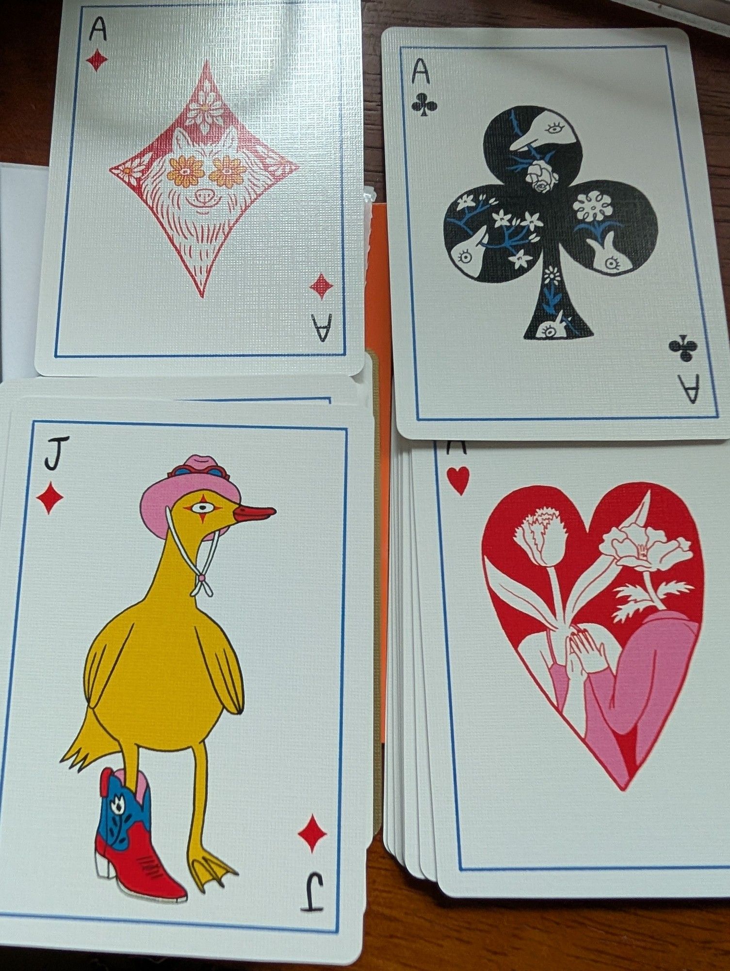 Four playing cards:
Ace of diamonds: like a dog or bear with flowers eyes. 
Ace of clubs: in each of the club leaves there is a dolphin with a flower
Ace of hearts: in a heart, two plant people are standing hand to hand
Jack of diamond: a little duck with harlequin eye wearing a fashionable pink hat and single cowboy booot