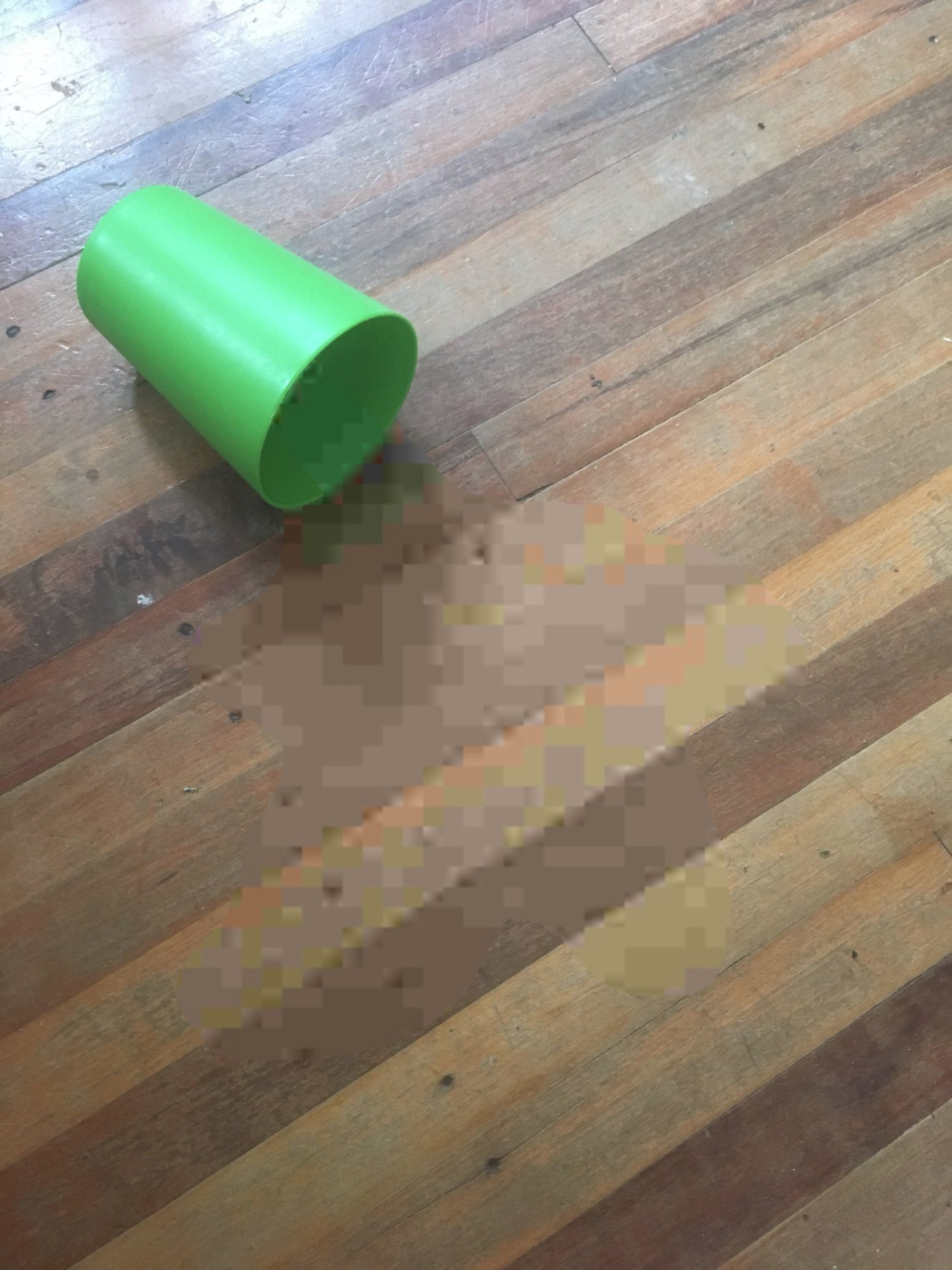 An image of a green plastic cup knocked over onto wooden floorboards. The center of the image, within an unclear blob, is heavily compressed and blocky, giving the appearance of a liquid "compression" that is spilt on the floor.