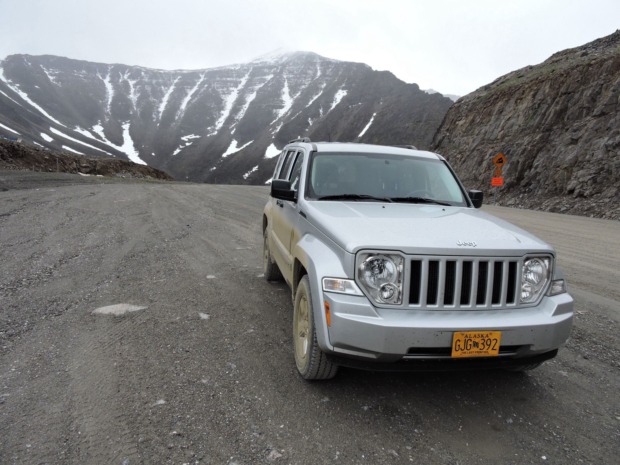 Der Atigun Pass in der Brooks Range ist der höchste Pass Alaskas. Ein silberner Jeep im Vordergrund auf der Passhöhe, im Hintergrund teilweise schneebedeckte Berge.