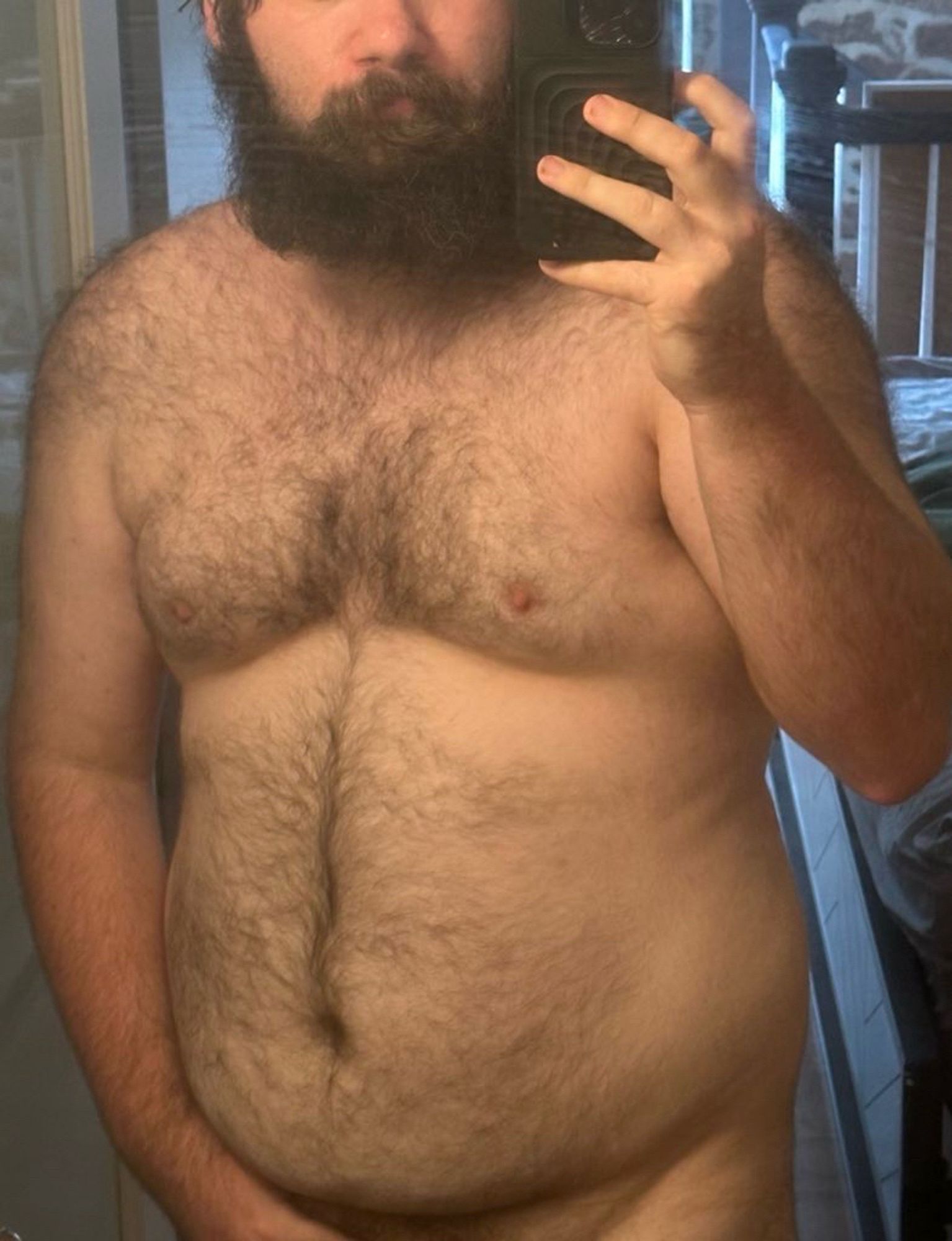 me, taking a mirror selfie. the photo cuts off at the waist and i am shirtless. you can see my body hair and my big beard.