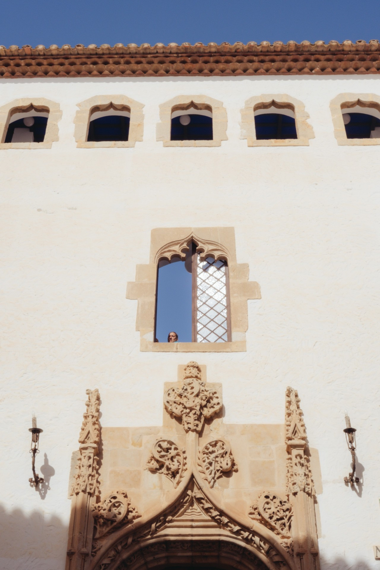 Fotografía de la fachada del Palau de Maricel de Sitges. En el centro de la composición hay una ventana abierta por la que asoma la cabeza un hombre (la estaba limpiando).