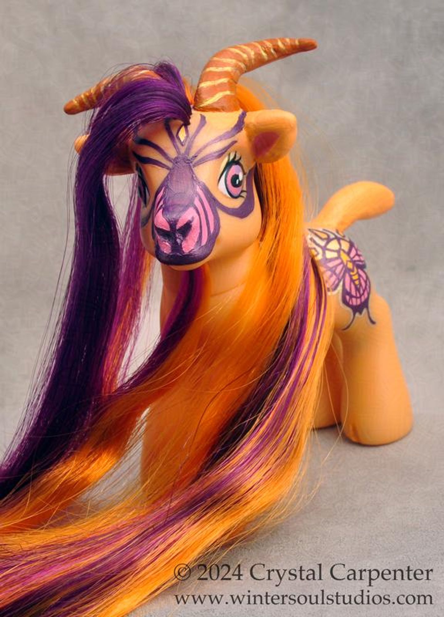 My little pony customized to be a goat. She's orange, with a gold and pink butterfly and sun cutie mark. Her long hair and beard are orange and purple.