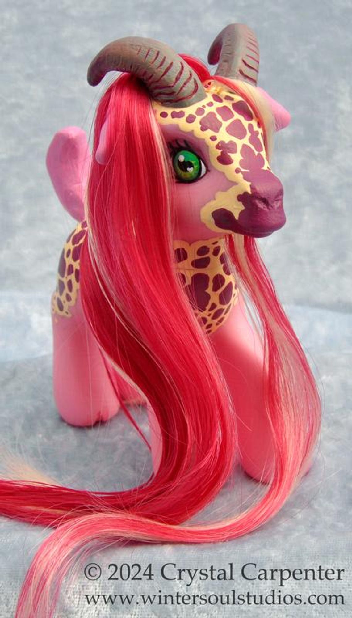 A customized My Little Pony figure - She's pink with goat ears, tail, and horns. She has the same patterns as found on a foxglove flower. Her long flowing hair and beard is mostly magenta with blonde highlights.