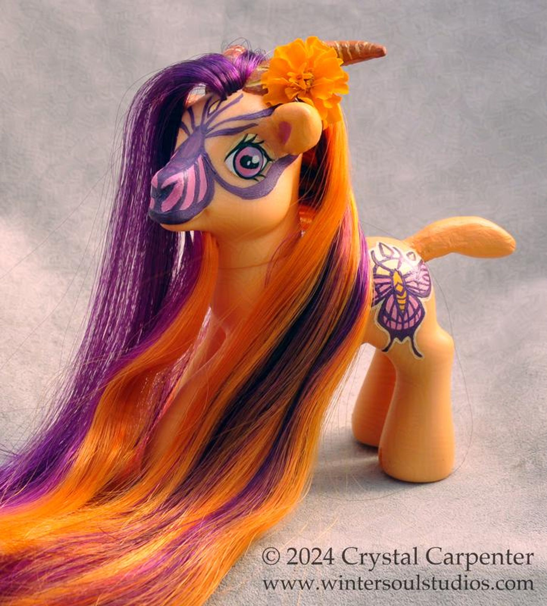 My little pony customized to be a goat. She's orange, with a gold and pink butterfly and sun cutie mark. Her long hair and beard are orange and purple.