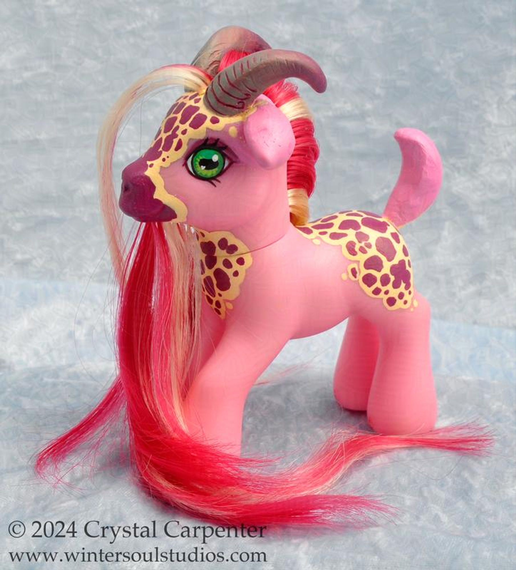 A customized My Little Pony figure - She's pink with goat ears, tail, and horns. She has the same patterns as found on a foxglove flower. Her long flowing hair and beard is mostly magenta with blonde highlights. Side view of the pony, to show the hand painted foxglove pattern.