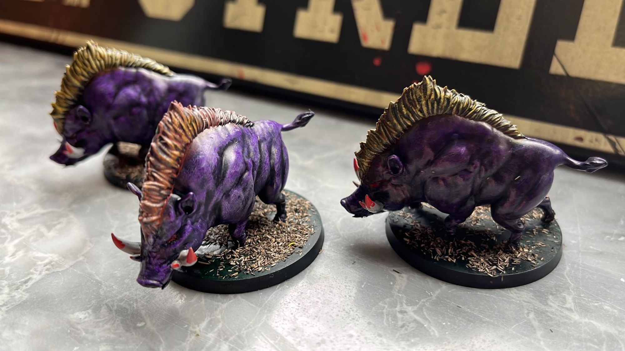 Three identical miniatures representing wild boar. Color scheme: purple skin, yellow hair. A bit of blood on their tusks.