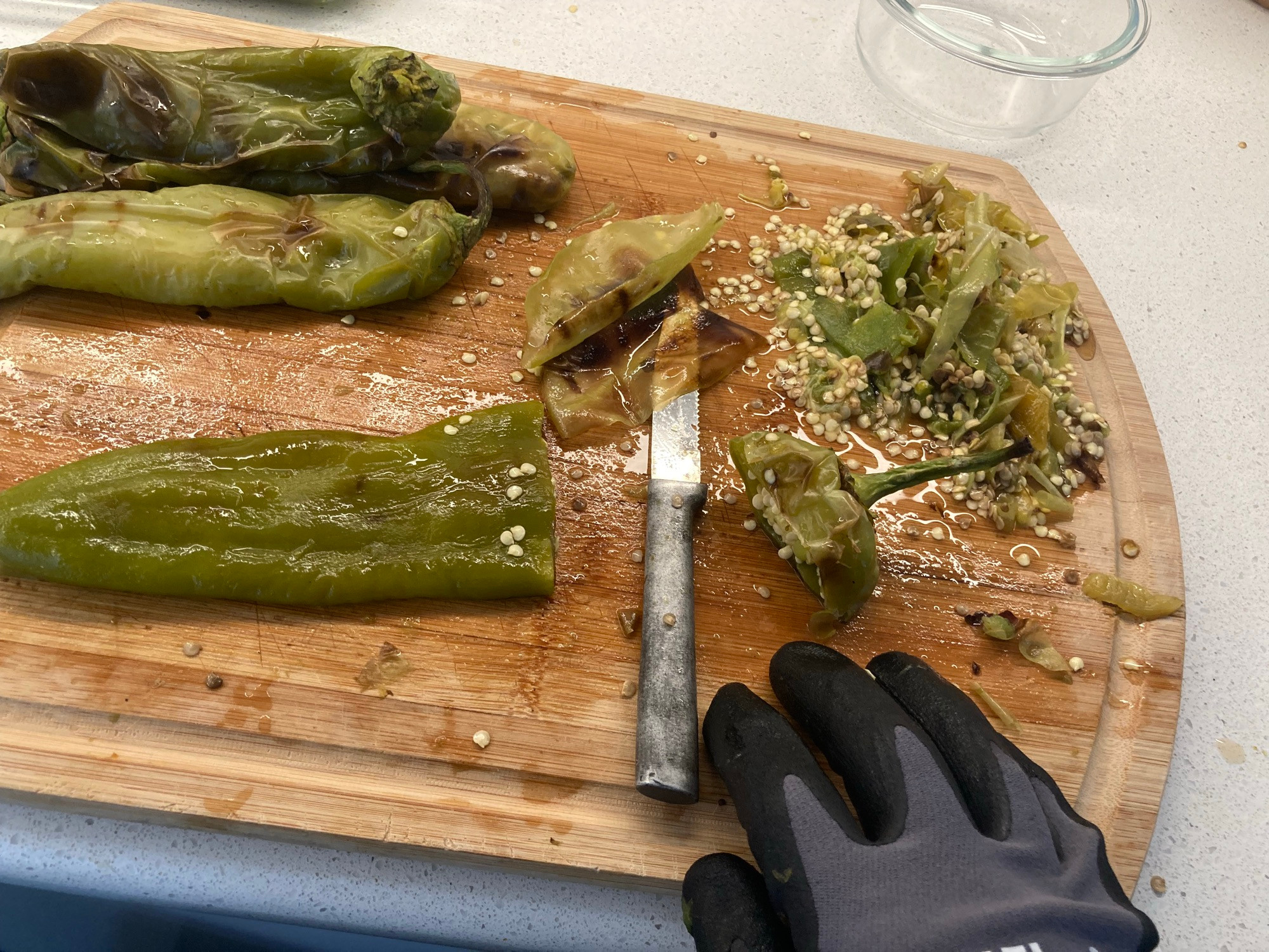 Cutting board showing a headless chile, a knife, the skin peeled off, and my garage-gloved hand