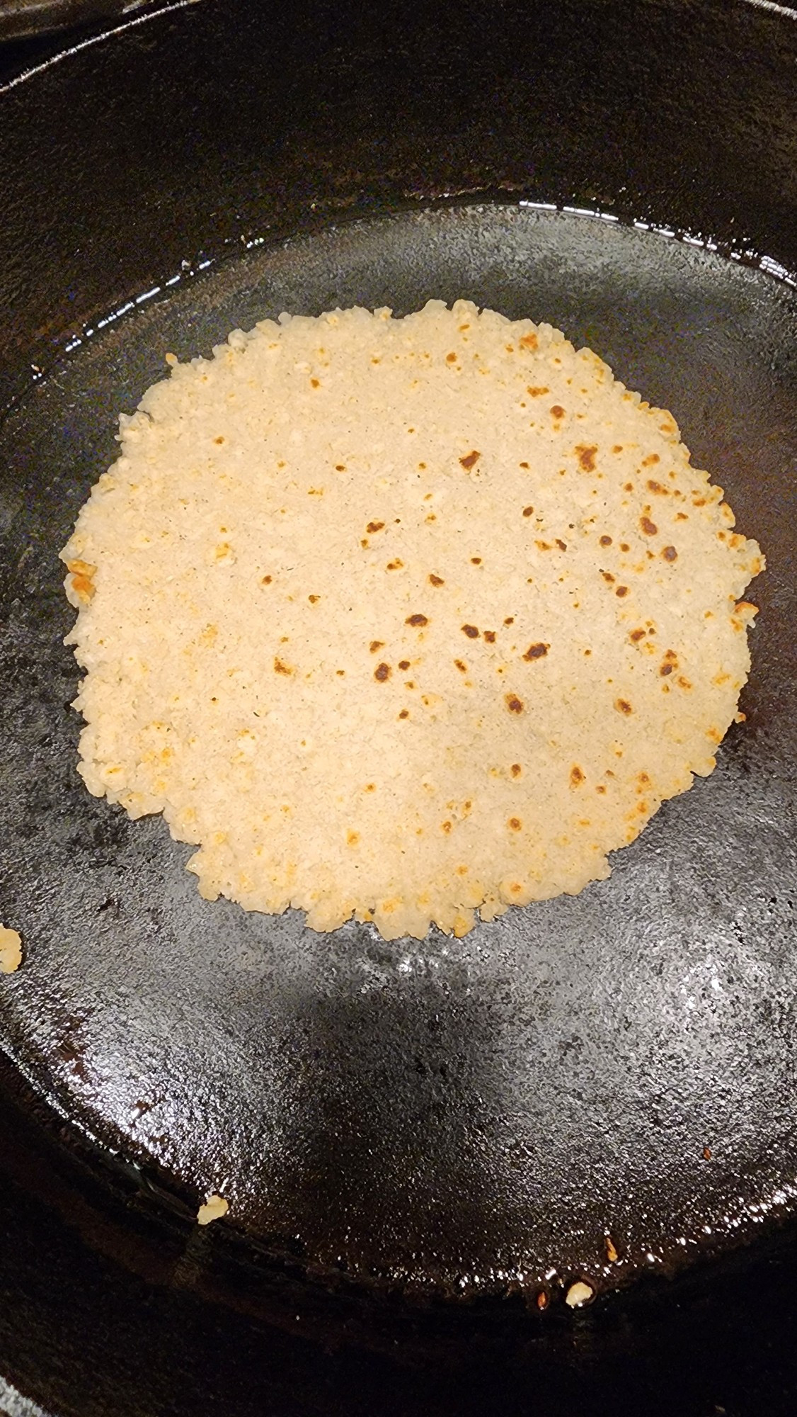 A reconstituted corn tortilla in a cast iron pan