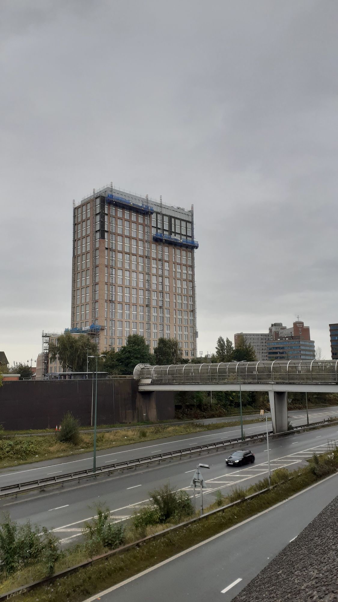 The building against a grey sky. Two working platforms are raised up near the top.