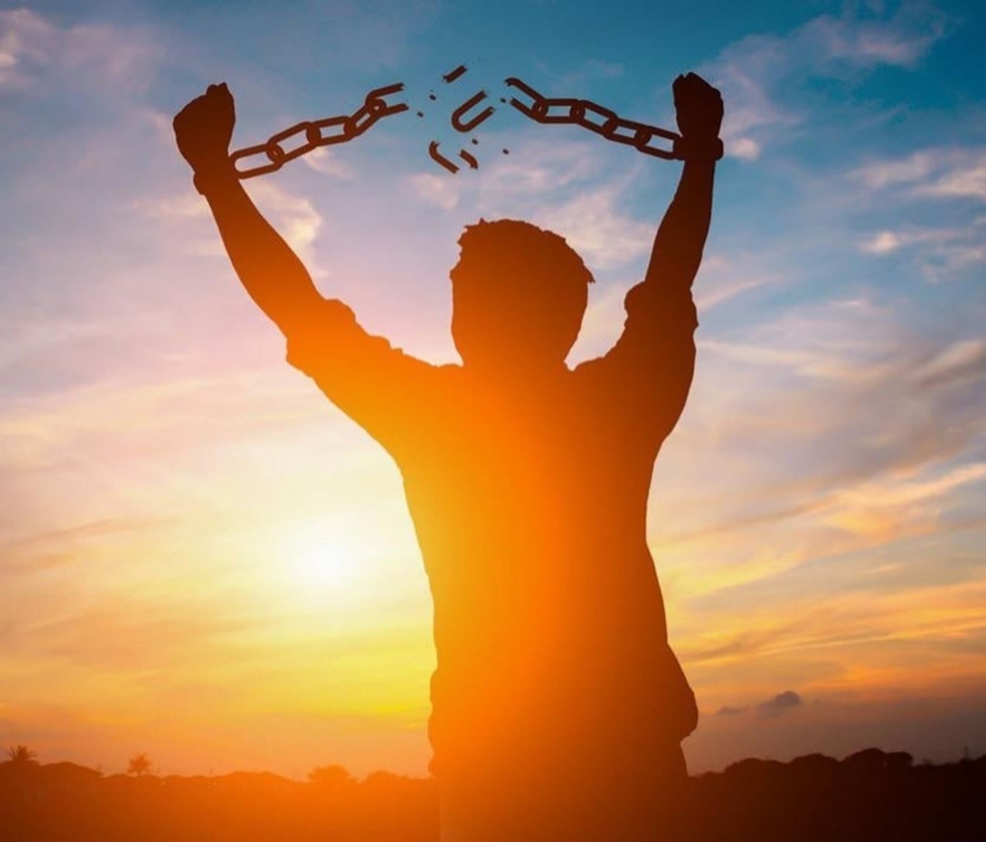 The image shows a silhouette of a person with their arms raised, breaking a chain. The background features a vibrant sunset with shades of orange and blue in the sky.