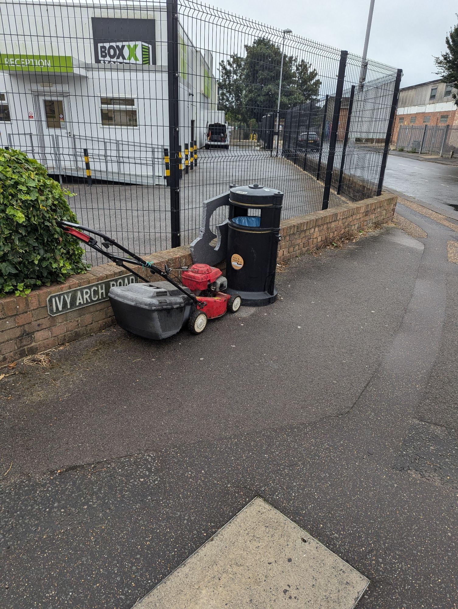 A lawnmower abandoned next to a bin.