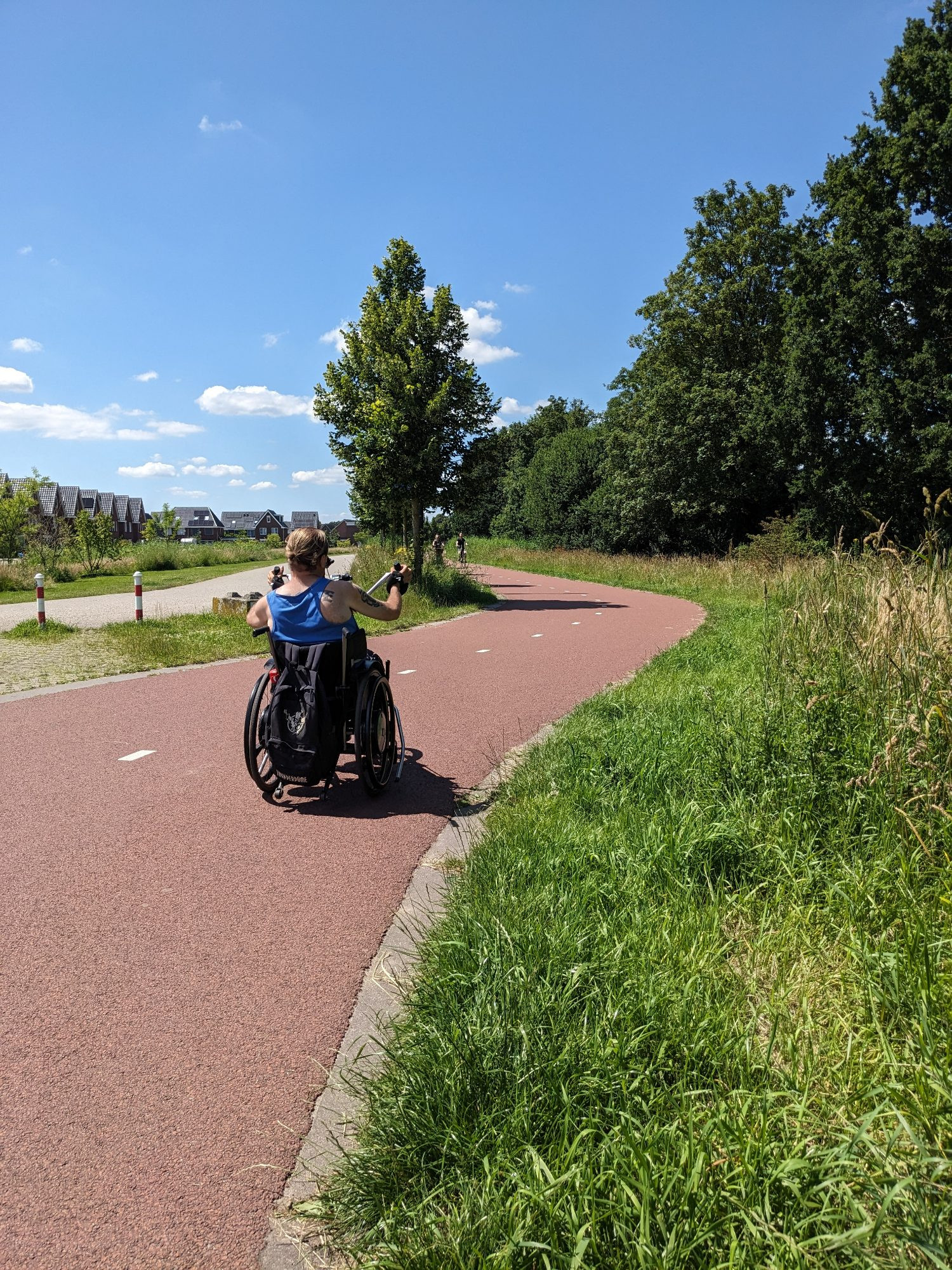 Ein Mann in einem Rollstuhl samt Handkurbel, mit der er sich leichter und schneller fortbewegen kann, auf einem rot asphaltierten Zweirichtungsradweg in den Niederlanden 