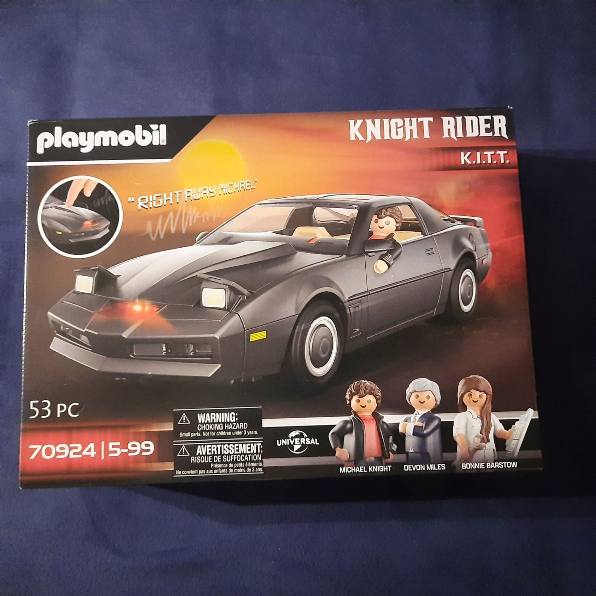 This is a Playmobil set featuring the iconic Knight Rider car, K.I.T.T. The box shows the sleek black car with its distinctive red light and features the three main characters from the show: Michael Knight, Devon Miles, and Bonnie Barstow. The tagline on the box is "Right Away Michael," a famous line from the show. The set includes 53 pieces and is recommended for ages 5 and up. The box also warns of choking hazards due to small parts. Overall, this Playmobil set is a must-have for any Knight Rider fan and offers a fun and engaging way to recreate scenes from the classic TV show.