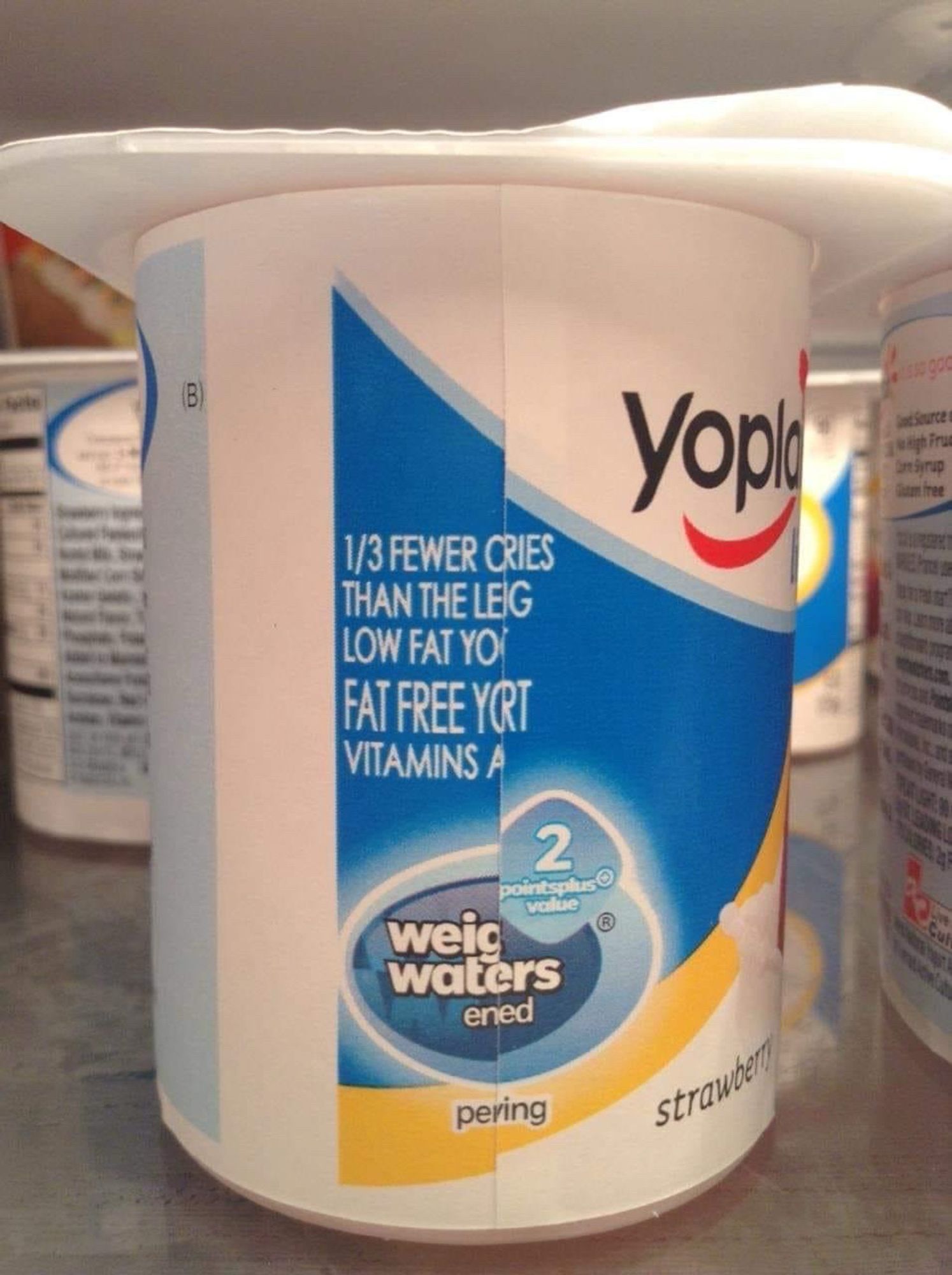 A busted/folded-over Yoplait yogurt label that looks like it says:

1/3 FEWER CRIES 
THAN THE LEIG 
LOW FAT YO
FAT FREE YORT 
VITAMINS A
weig waters
ened
pering