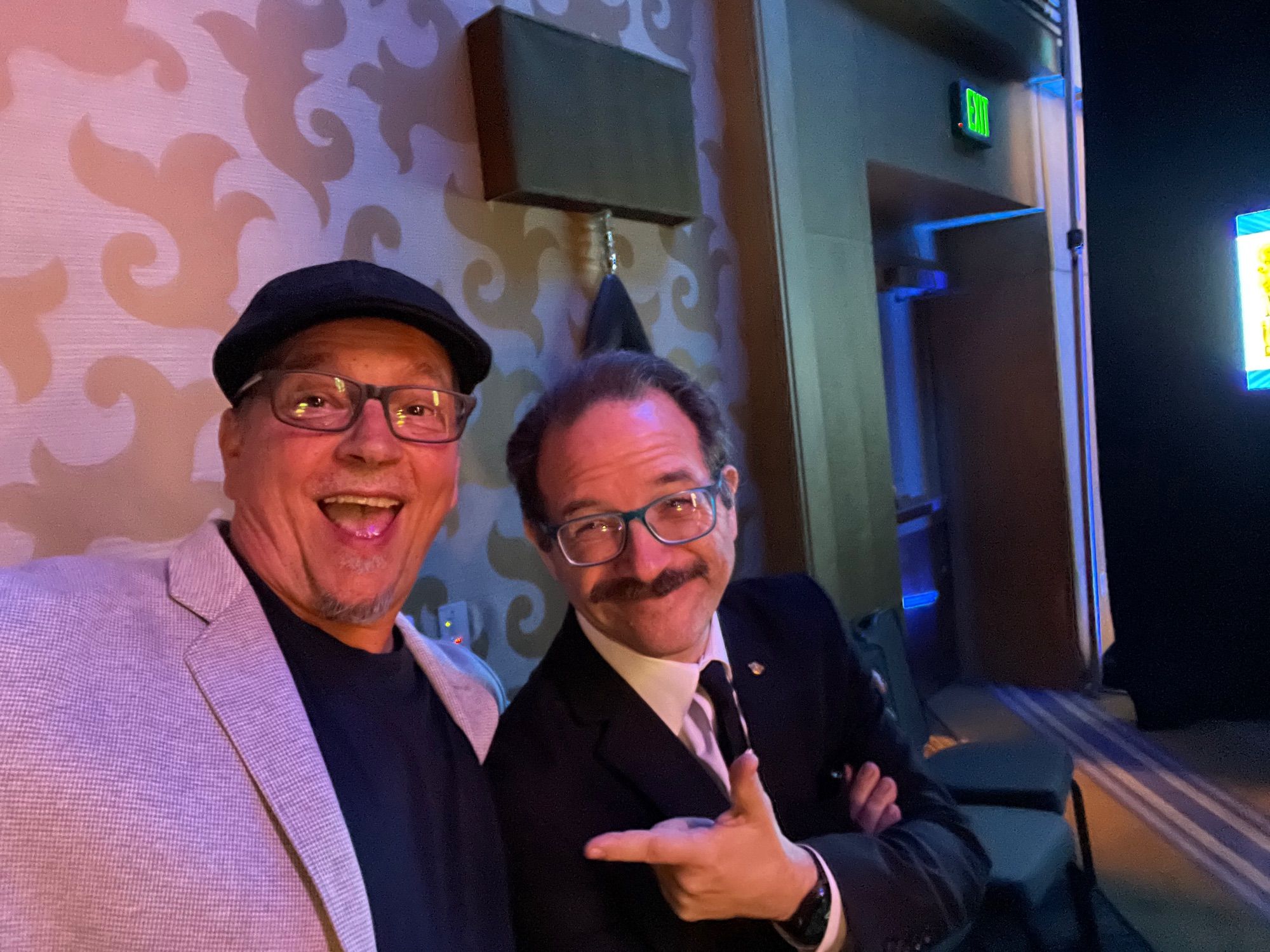 Two white male middle aged comic book creators smiling backstage, preparing to go on.