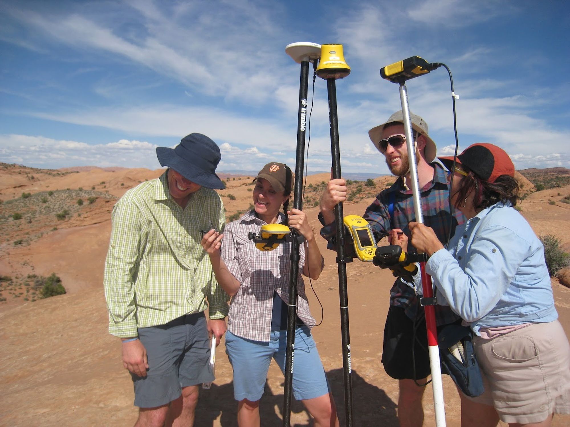 Photo of four people in a bedrock landscape with three survey poles and assorted instruments