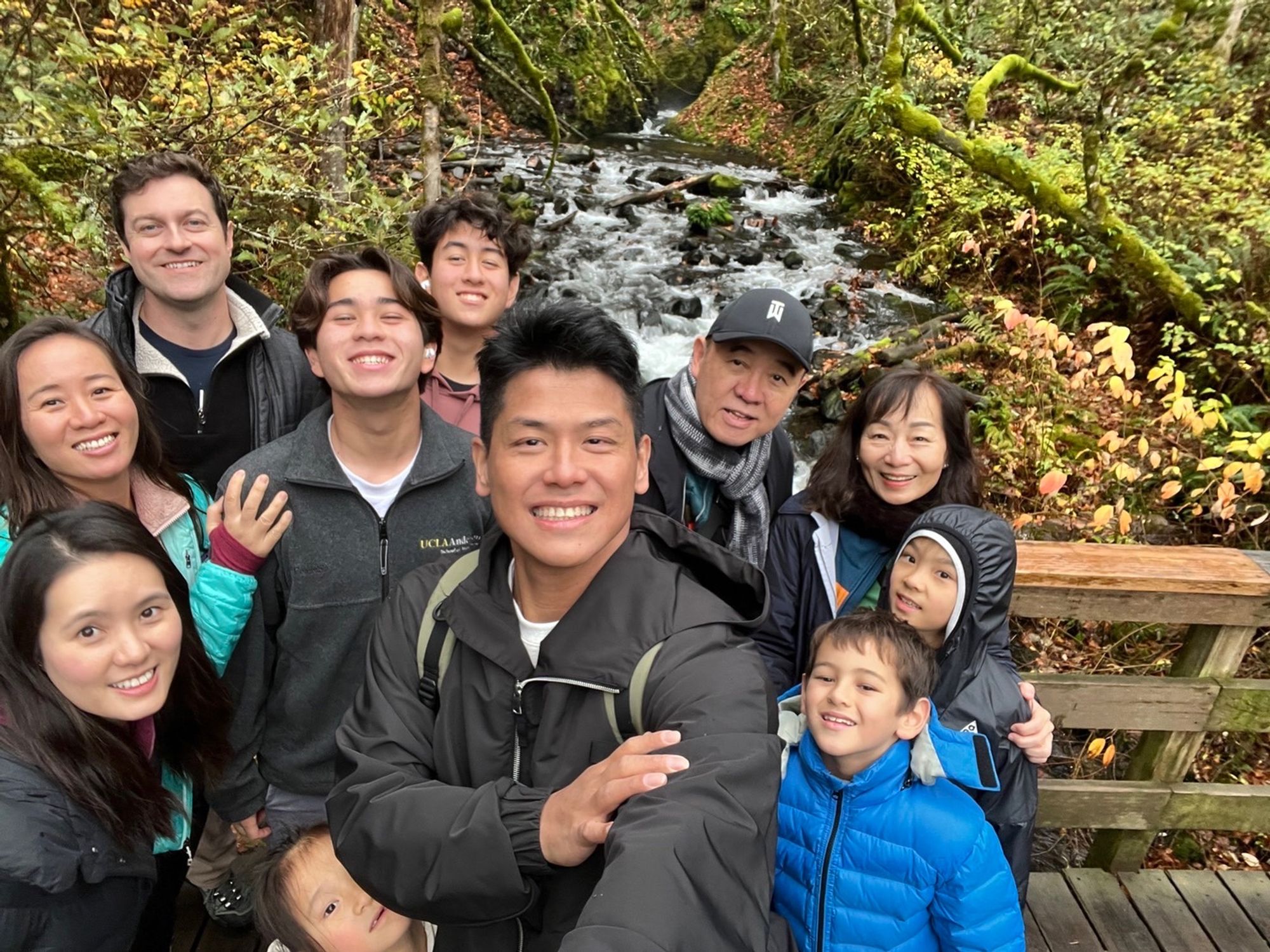 A multigenerational family taking a group selfie on a bridge beside a stream