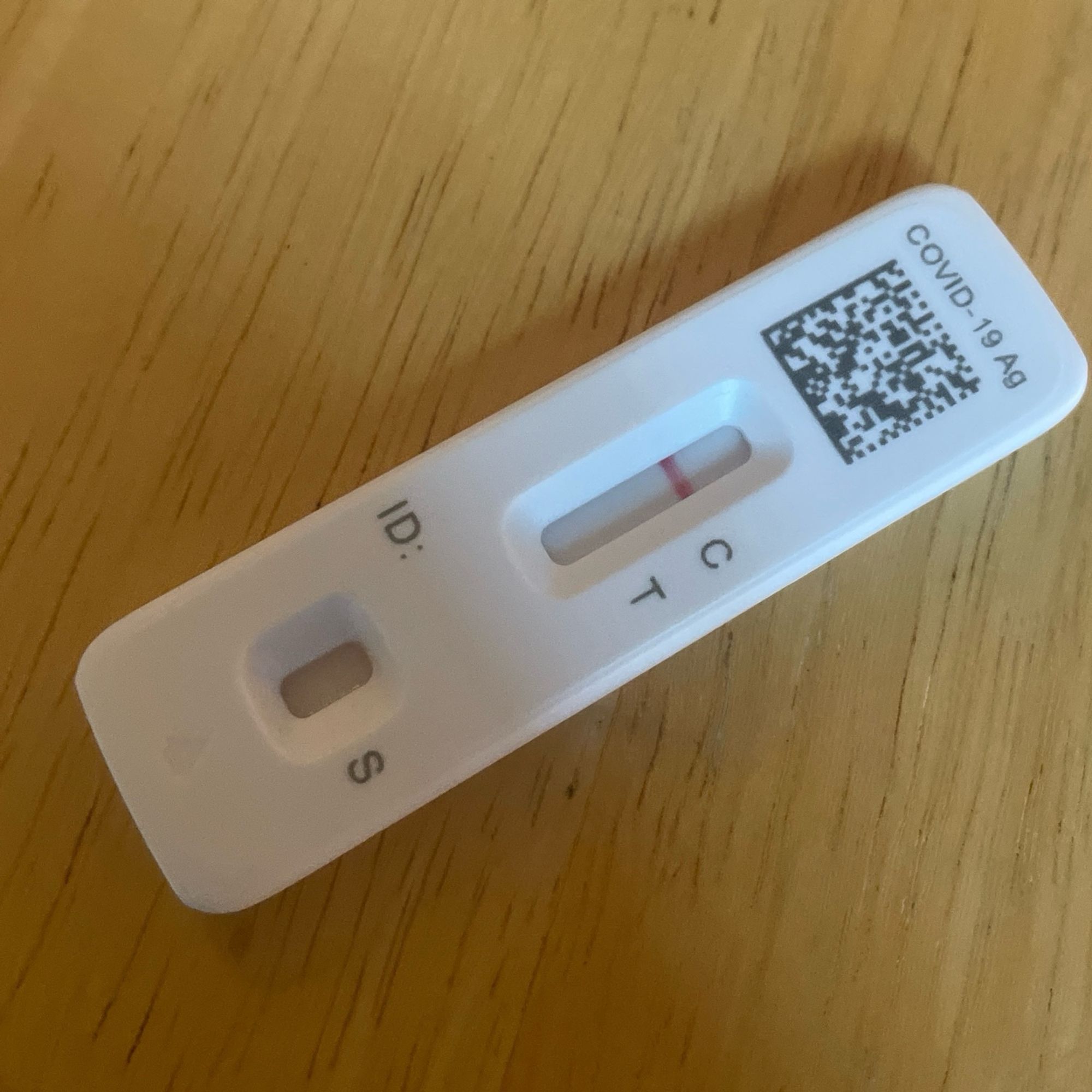 A flowflex brand COVID-19 test rests on a wooden table. The test is showing negative