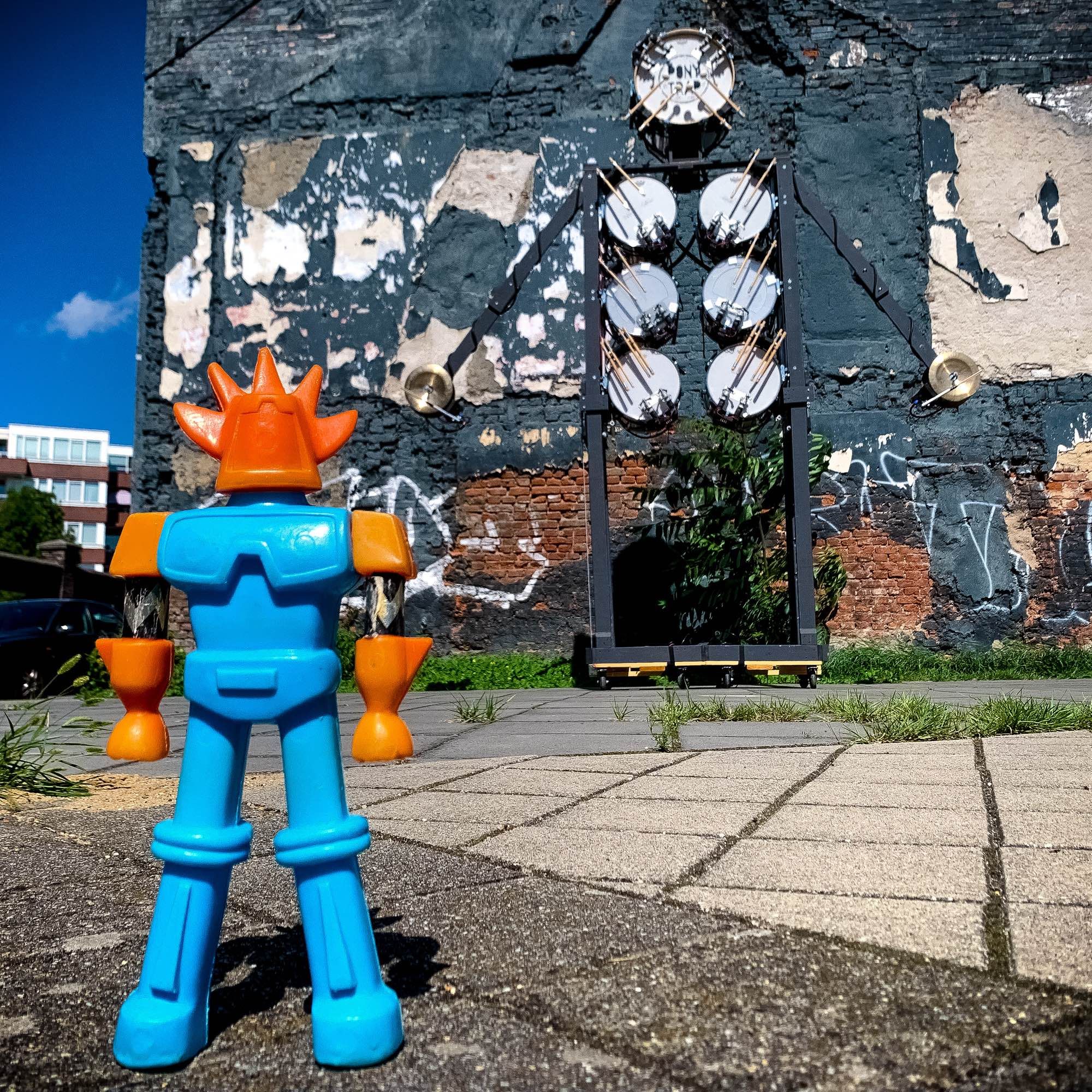 A vintage blow-mold Getter Dragun knockoff toy stands in front of a 5 meter tall drumming robot shaped like a scarecrow.