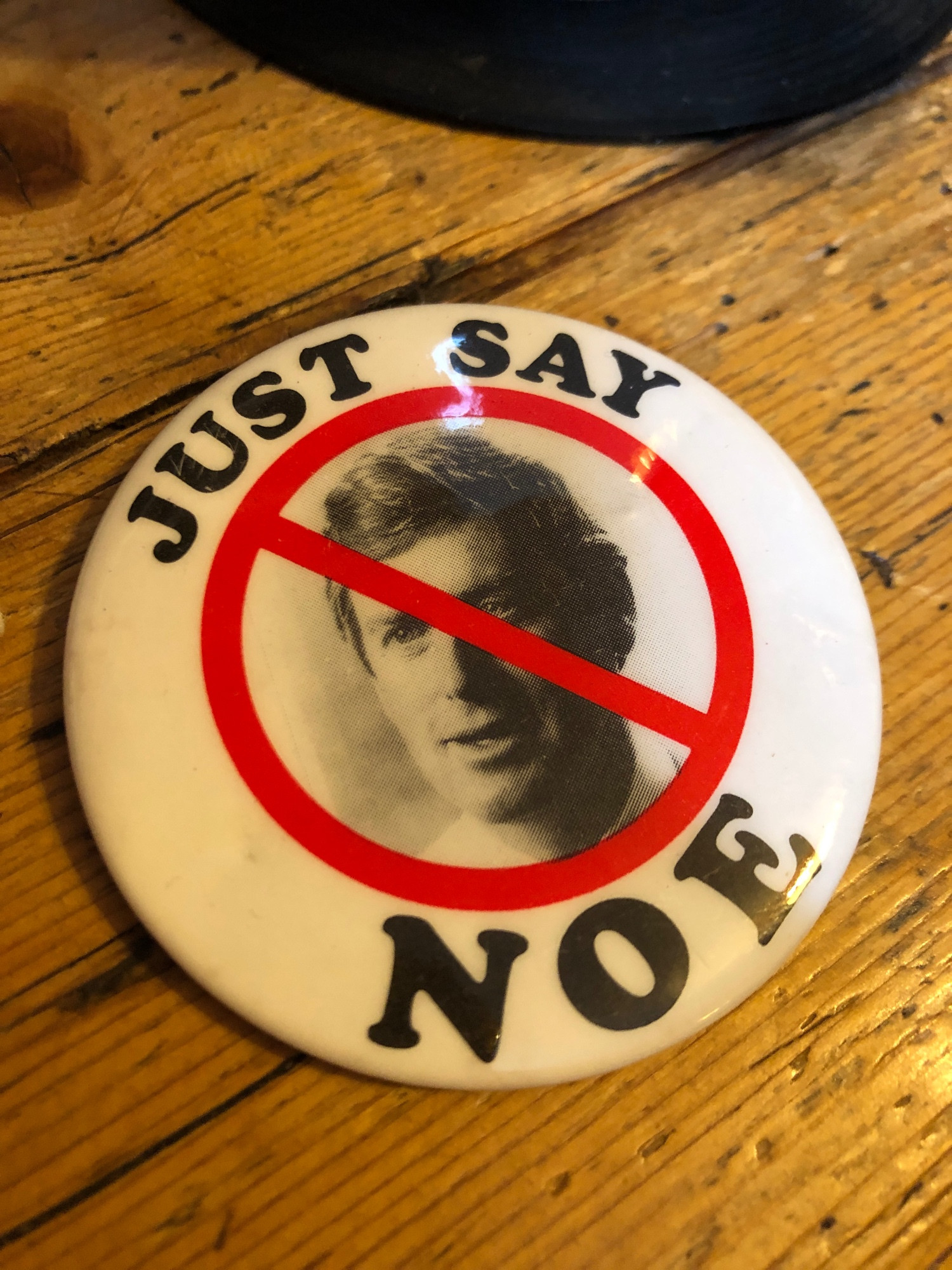A badge with a photo of a man crossed out with the slogan 'just say noe' - no with an E. It is Dan Quayle, vice president of the United States who famously mis-corrected a child's spelling of 'potato'.