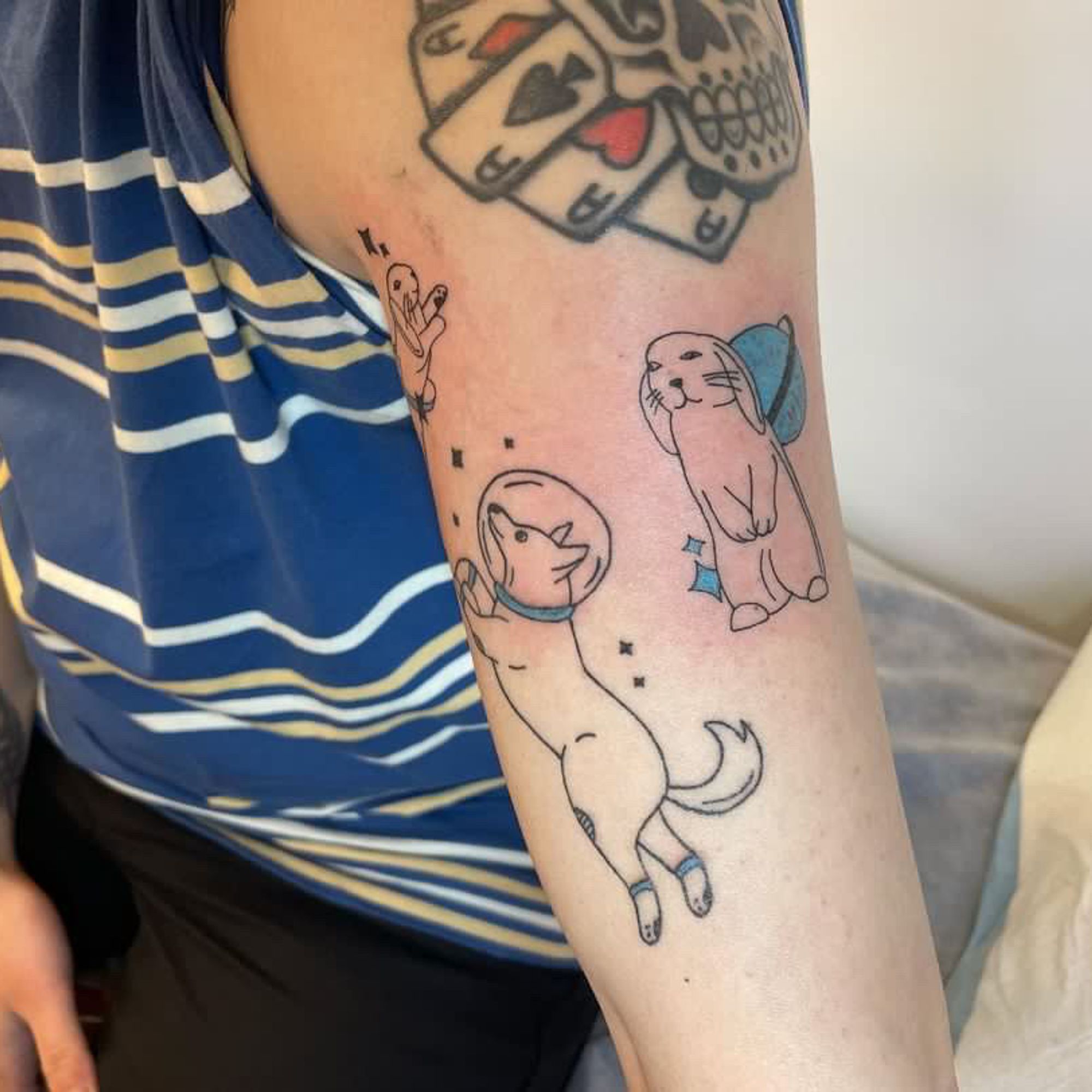 Photo of Pup Alexx's arm with a tattoo of a Dog with a space helmet, a Rabbit standing on it's back legs and a skull with some playing cards 