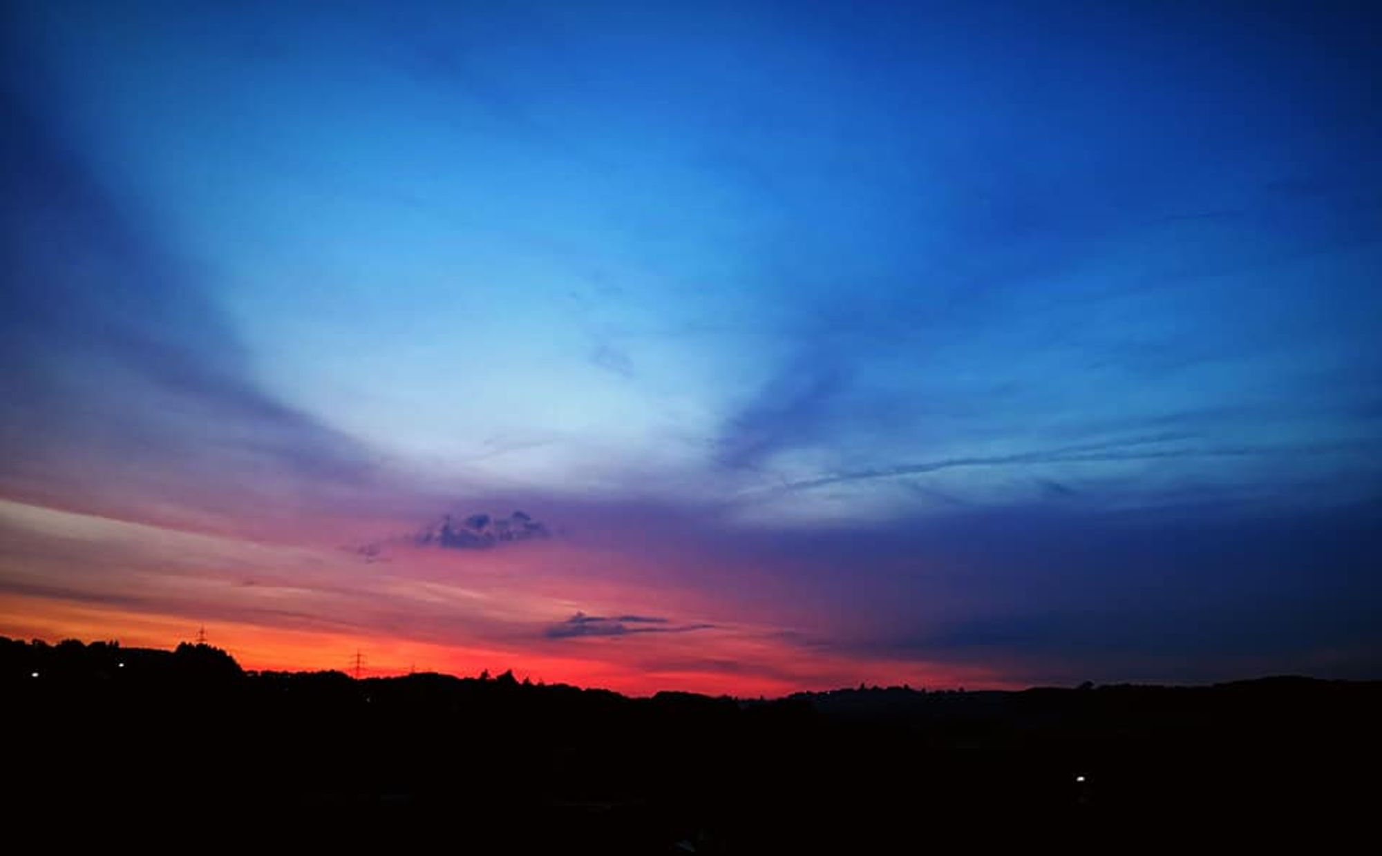 Sonnenaufgang - Die Sonne ist noch nicht zu sehen, aber sie mal bereits einen Streifen des Himmels am Horizont orange. Darüber ist der Himmel blau. Es ist ganz leicht bewölkt.