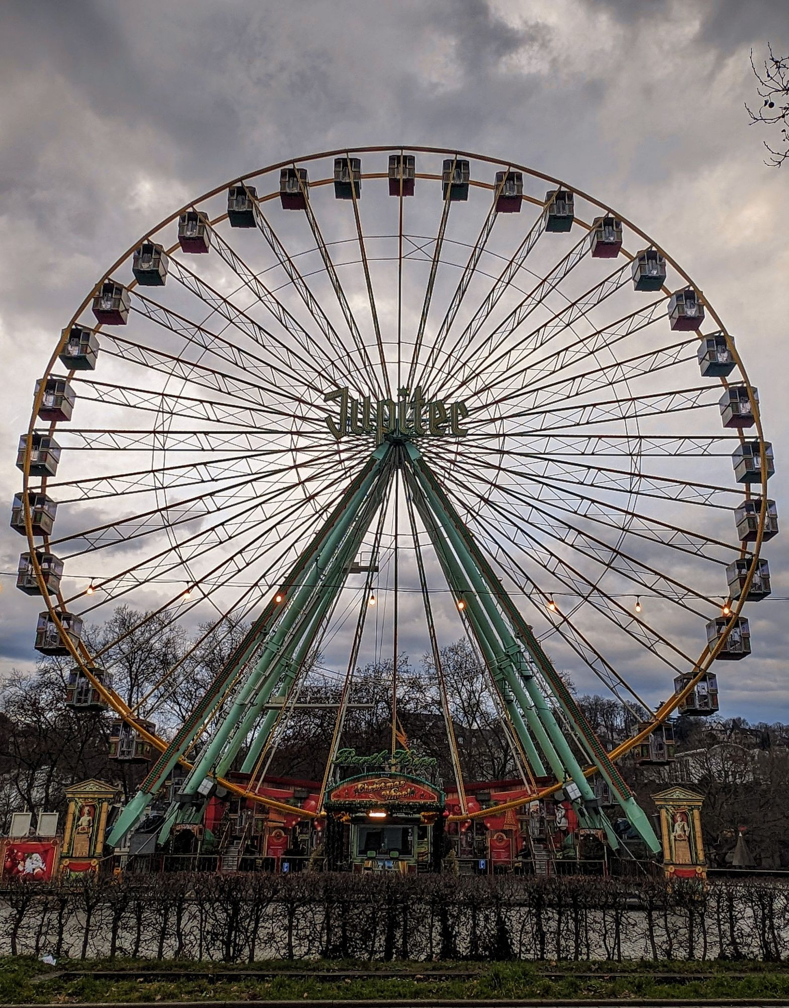 Ein Riesenrad vor bedecktem Himmel. In der Mitte des Rades steht Jupiter.