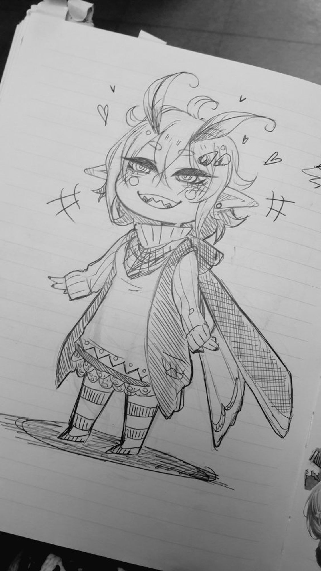 a photo of a ballpen doodle on a notebook. the drawing shows my oc menma in chibi style. she is smiling widely and there are hearts flying next to her head. you can see her full body, she is dressed in a lot of layers. since she is a moth character, she has antennas on her head and wings on her back.