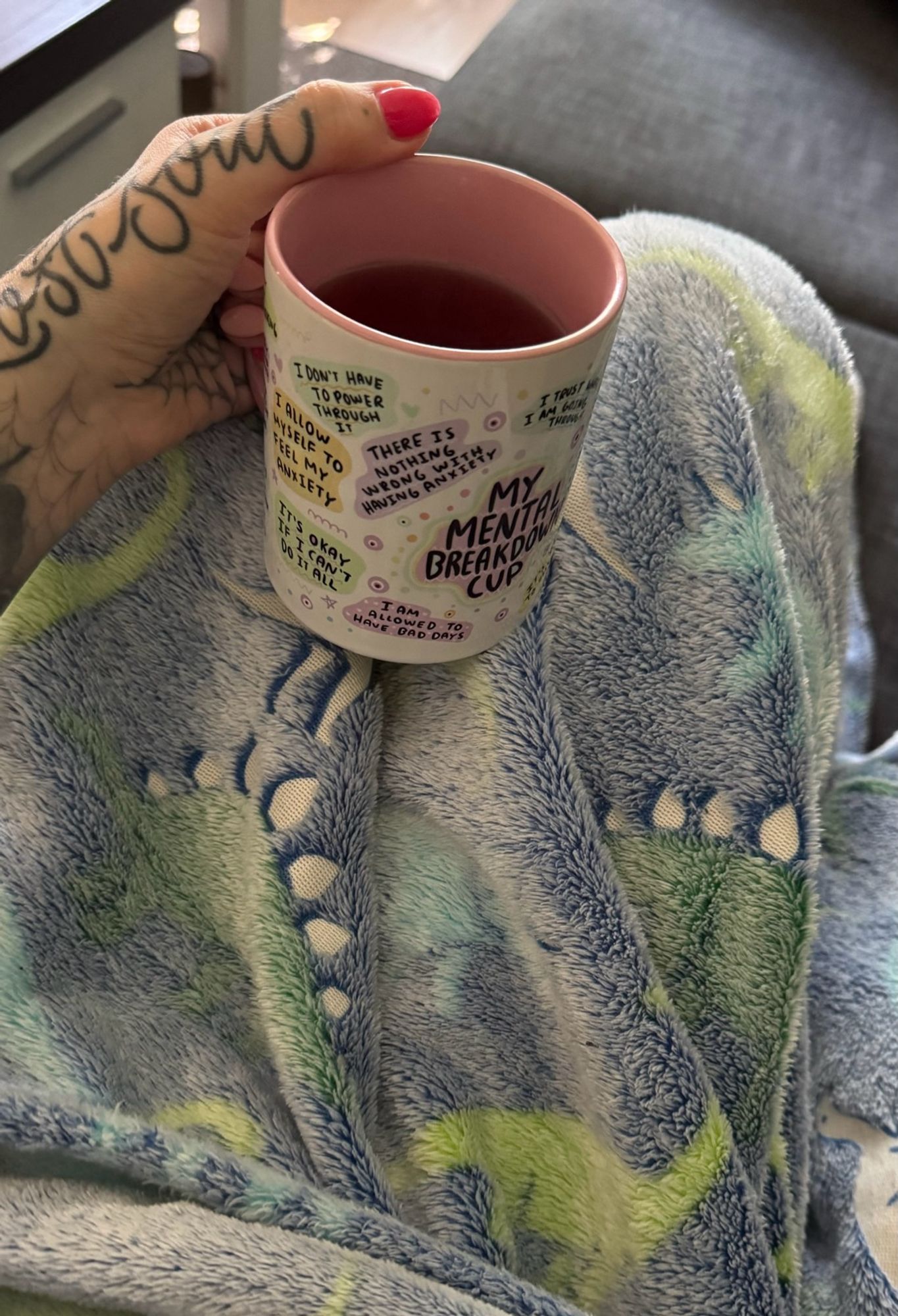 POV Halte eine Teetasse in der Hand, abgestürzt auf meinen Beinen. Bin zugedeckt mit einer Dino Kuscheldecke und sitze auf dem Sofa.