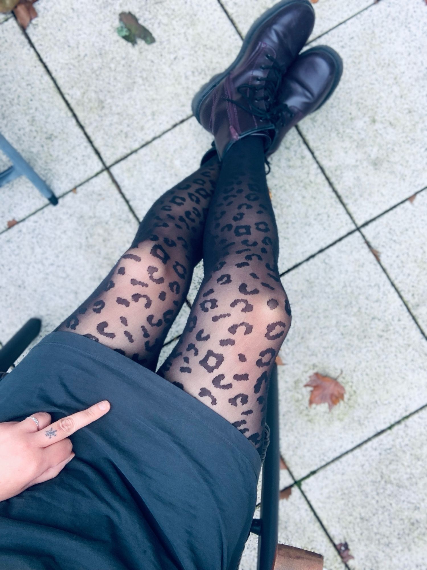 Foto von meinem Unterkörper. Ich trage lila Boots, eine Leoprint Strumpfhose und ein kurzes, dunkelgrünes Kleid. Auf meinem linken Bein liegt meine Hand mit ausgestrecktem Mittelfinger.