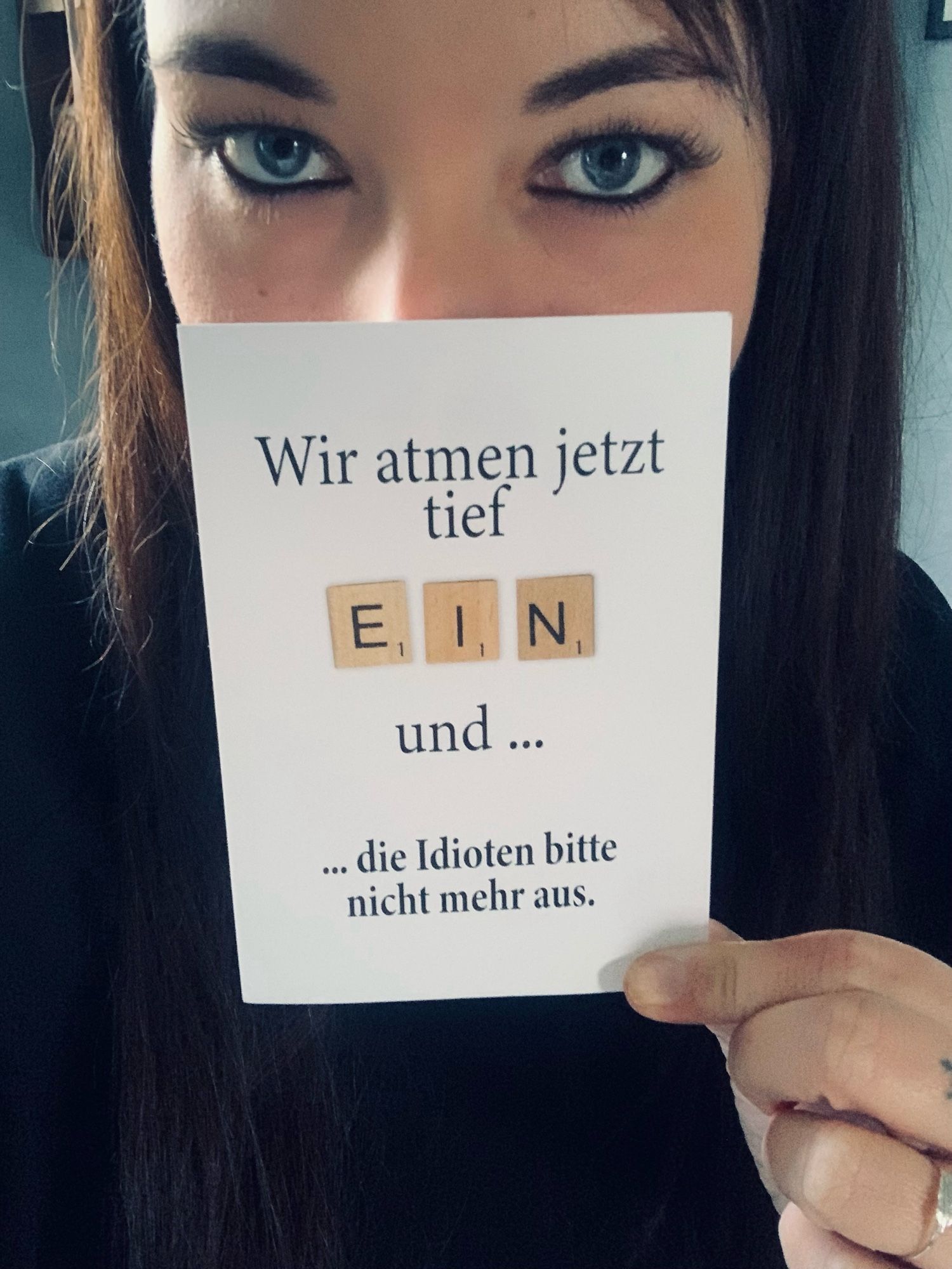 Selfie. Man sieht mein Gesicht bis knapp über der Nase, mit meiner linken Hand halte ich eine Postkarte vor mein Gesicht. Aufschrift: „Wir atmen jetzt tief ein und… die Idioten bitte nicht mehr aus“