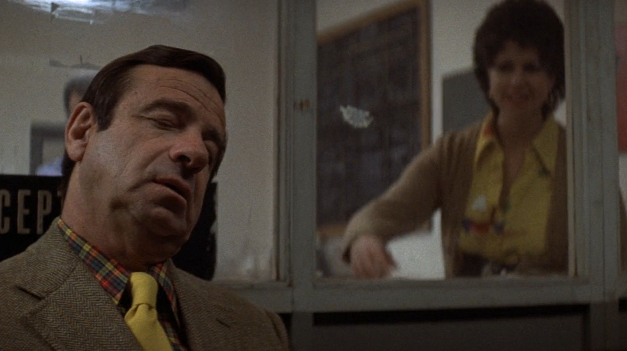 Walter Matthau asleep sitting up, his head resting against a window, with a woman behind the window trying to get his attention