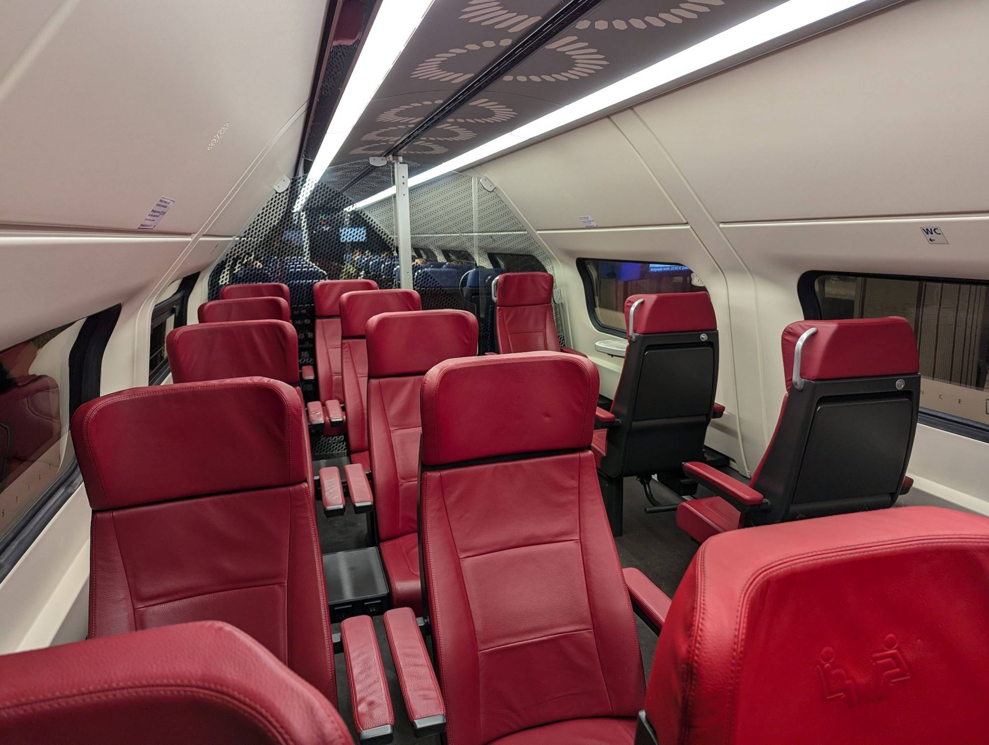 Train interior with all empty red first class seats in the foreground and blue seats behind the glass. It is the upper deck of a renovated VIRM train.